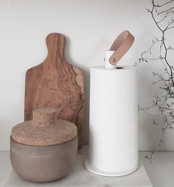 Hvid køkkenrulleholde med rund en rund fod. I toppen er der en læderstrop i naturfarve.