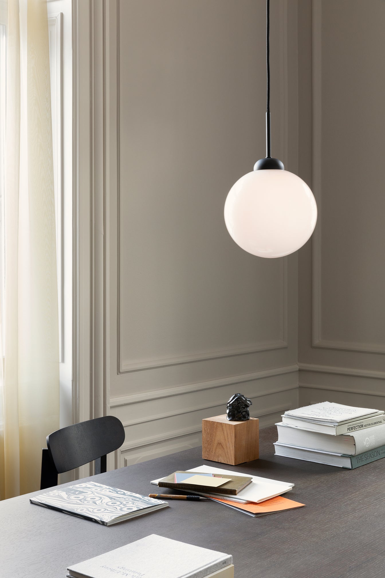 Pendel bestående af en rund skærm af opalglas og sort fatning samt ophæng, hængende over skrivebord