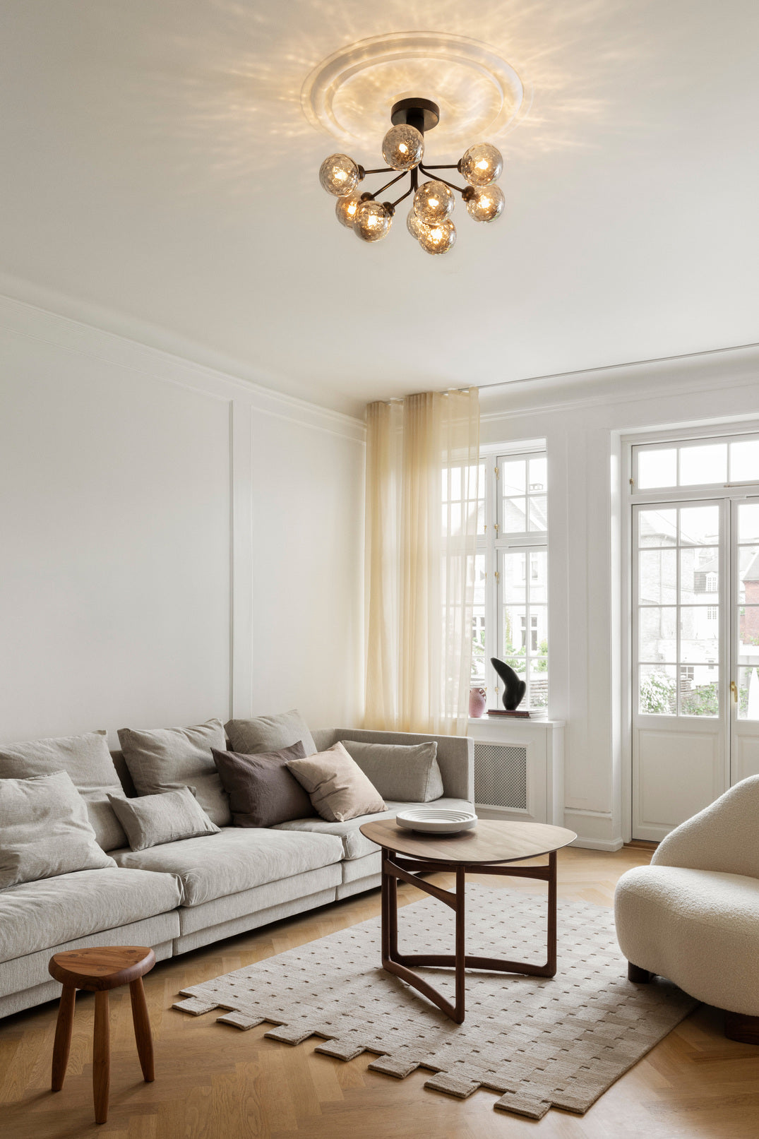 Lysekrone bestående af runde skærme i røgfarvet optikglas samt sort krone, i dagligstuemiljø