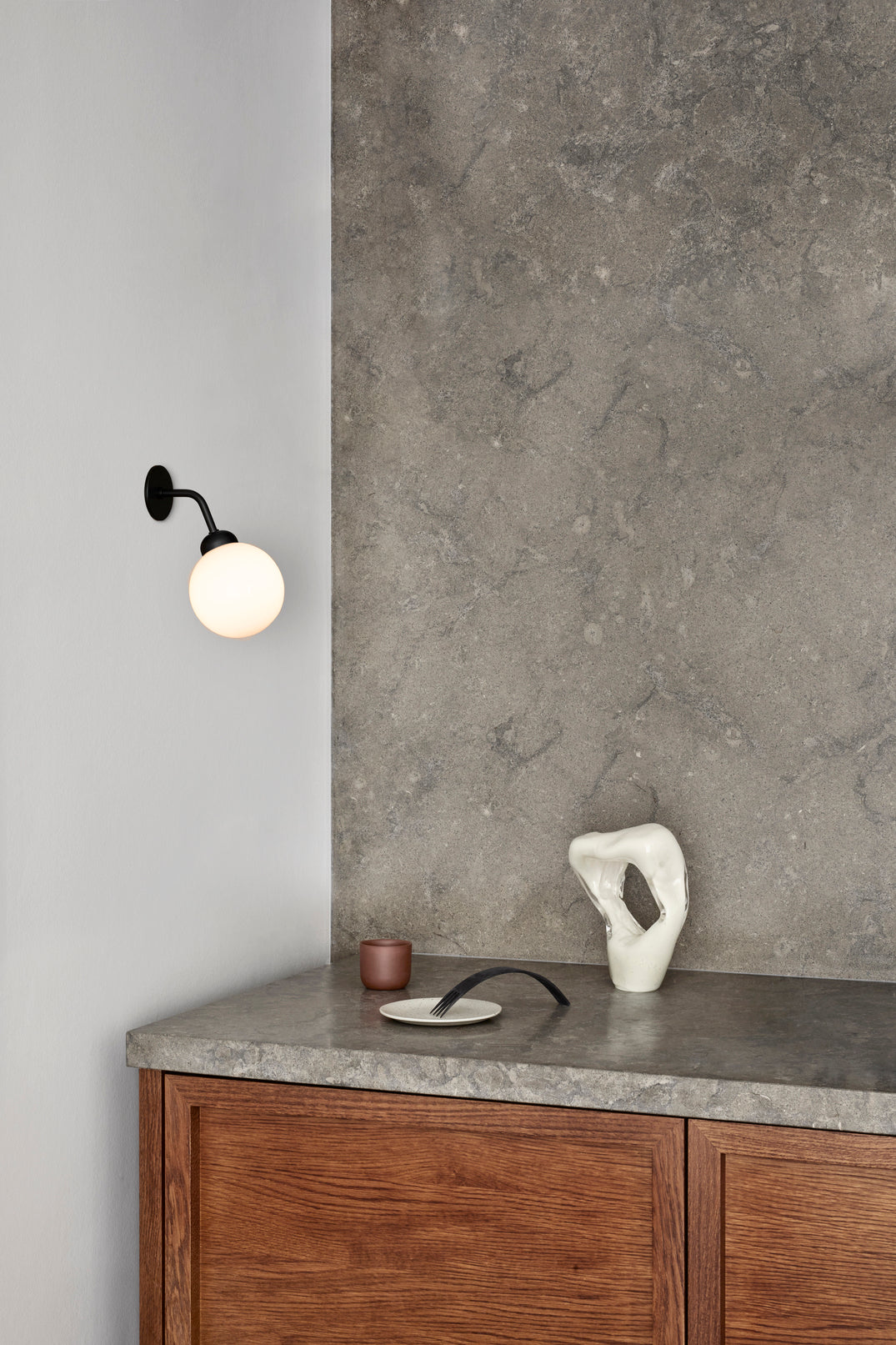 Væglampe med rund skærm af opalglas og sort stel, på hvid væg ved siden af køkkenbord