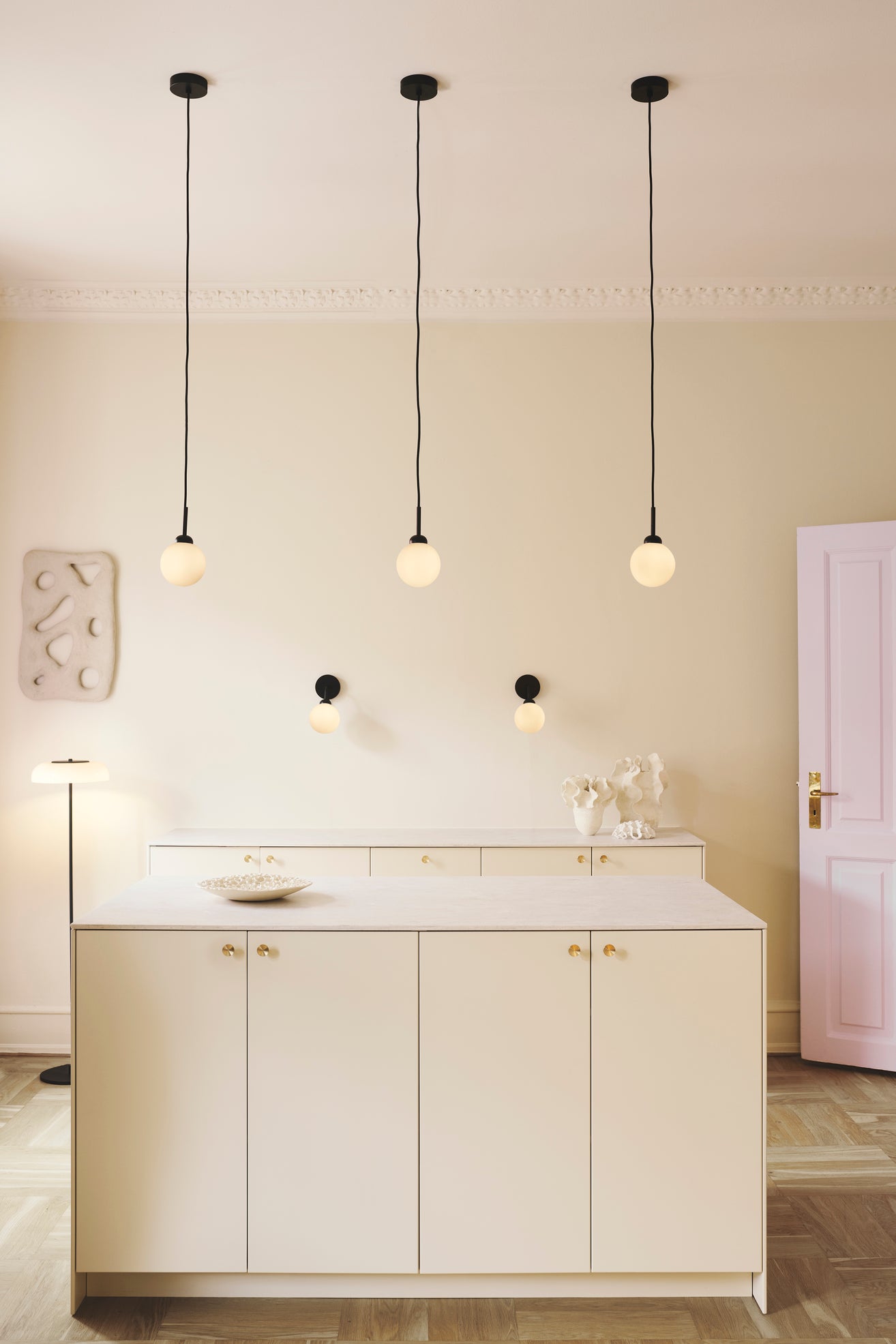 To væglamper med rund skærm af opalglas og sort stel, hængende over køkkenbord