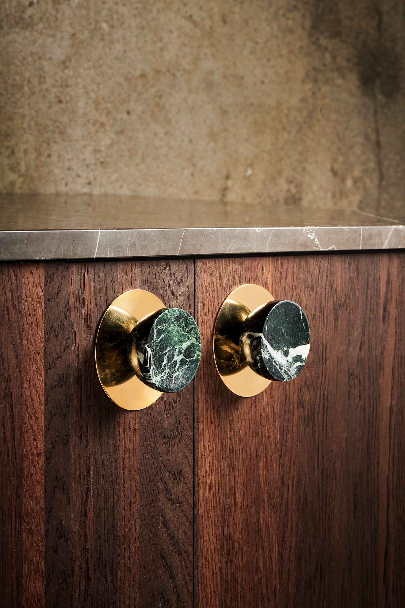 Her ses messingbagpladen monteret bag Get at grib møbelknopperne i grøn marmor.