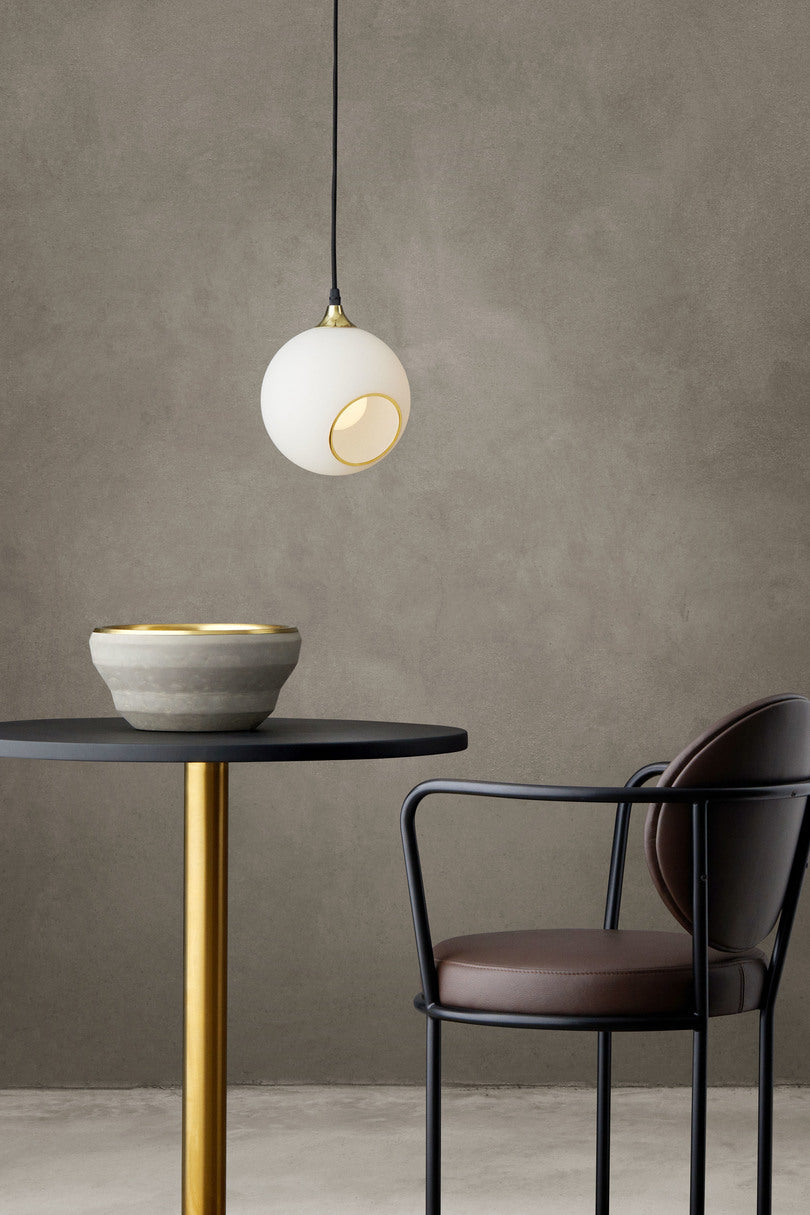 Rund lampe i hvidt glas og med et afskåret stykke med guldkant og kig til pæren. Fatning og rosetten er guldfarvet og ledningen er af sort stof.