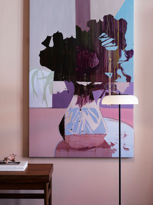 Gulvlampe med sort stel og fatning samt glasskærm i opalglas, i dagligstuemiljø