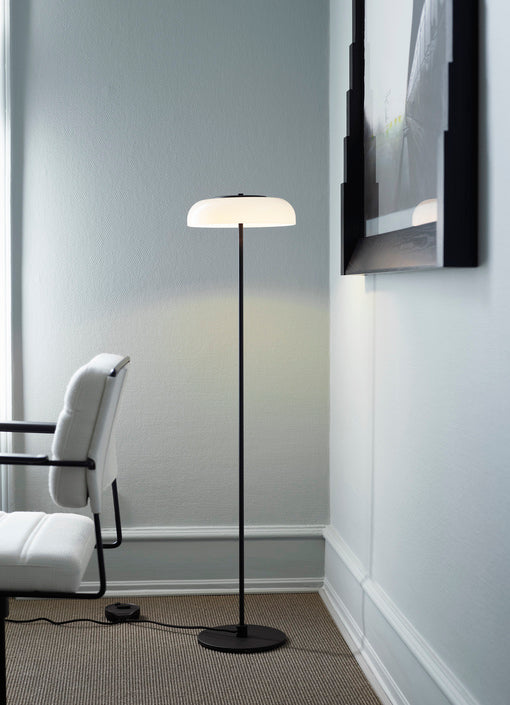 Gulvlampe med sort stel og fatning samt glasskærm i opalglas, i dagligstuemiljø