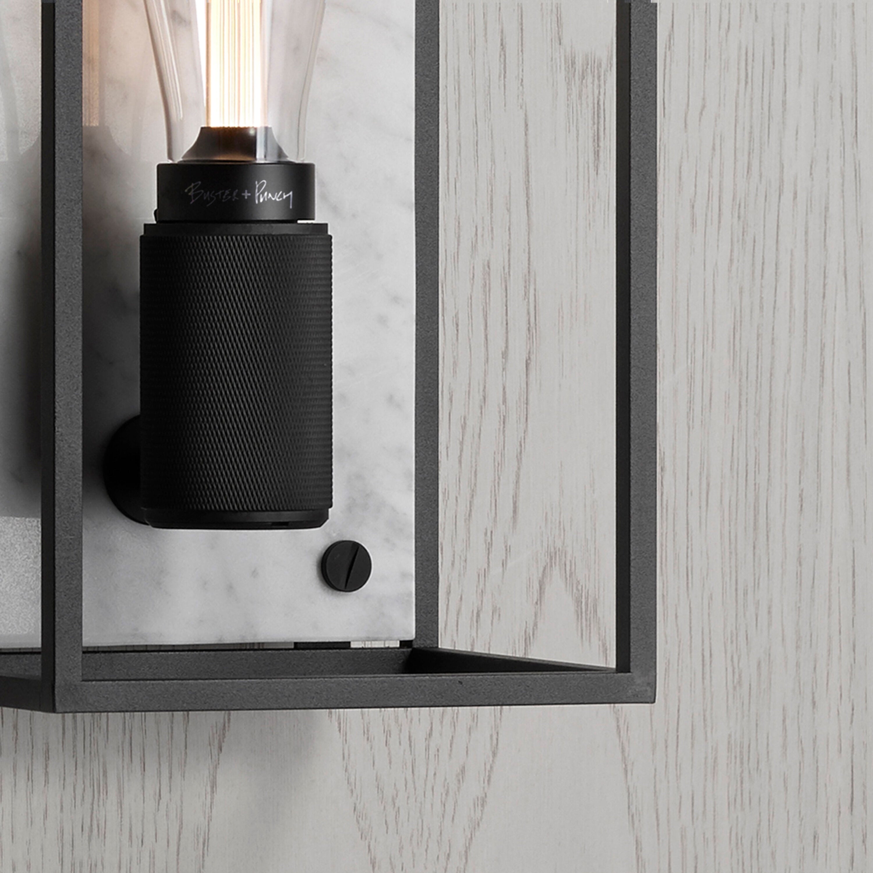 Buster and Punch caged wall lamp medium i sort metal med bagpanel i hvid marmor.