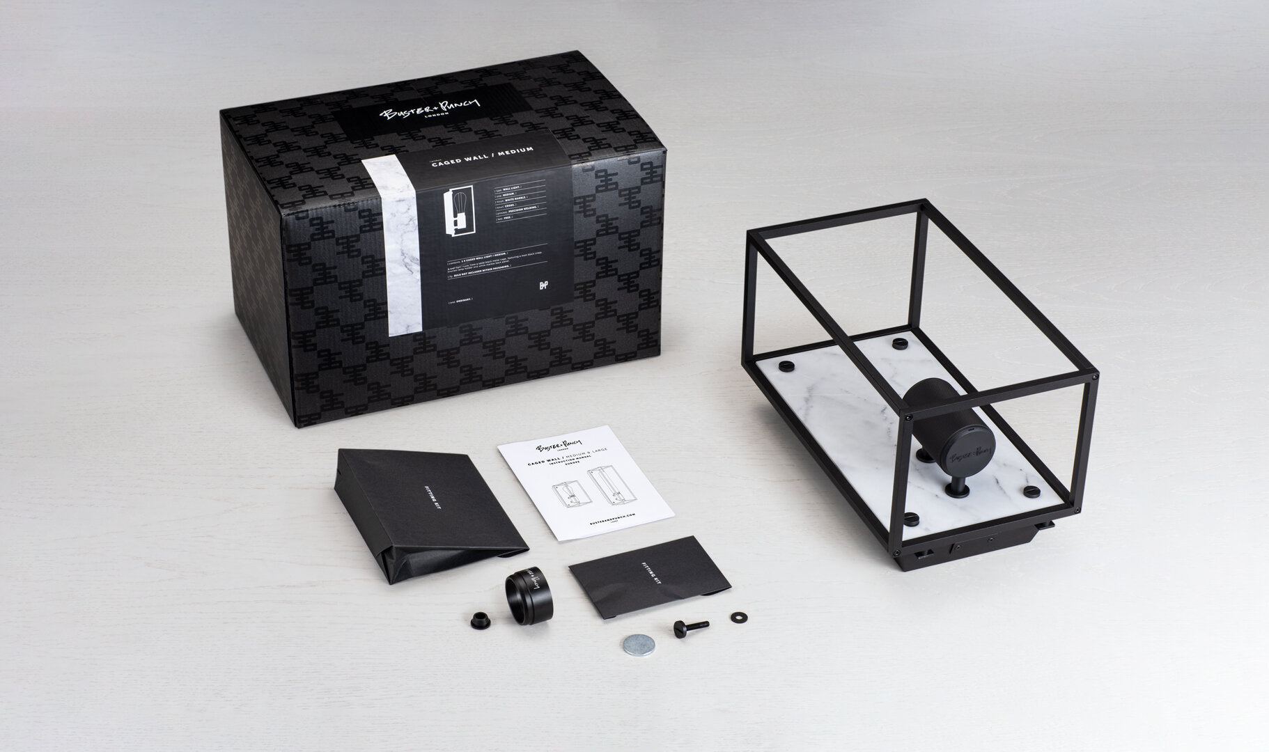 Buster and Punch caged wall lamp medium i sort metal med bagpanel i hvid marmor.