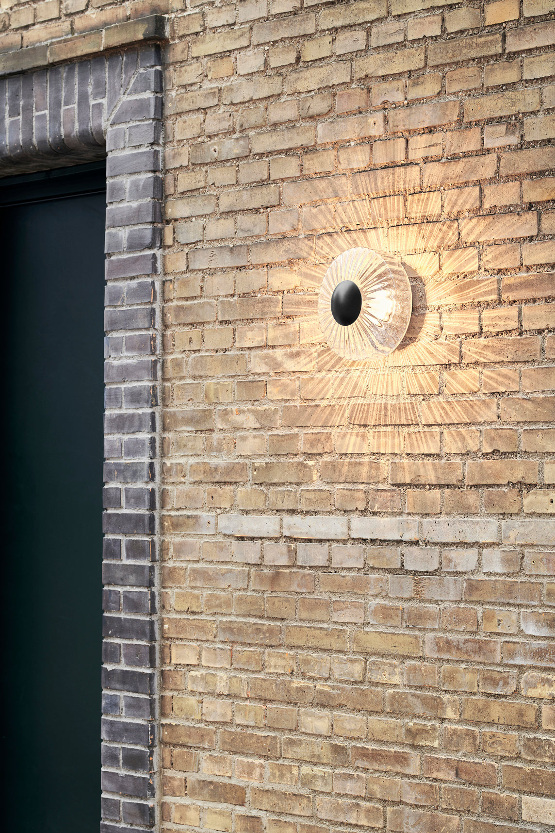 Rund udendørs væglampe af klart glas, på mur af gule mursten