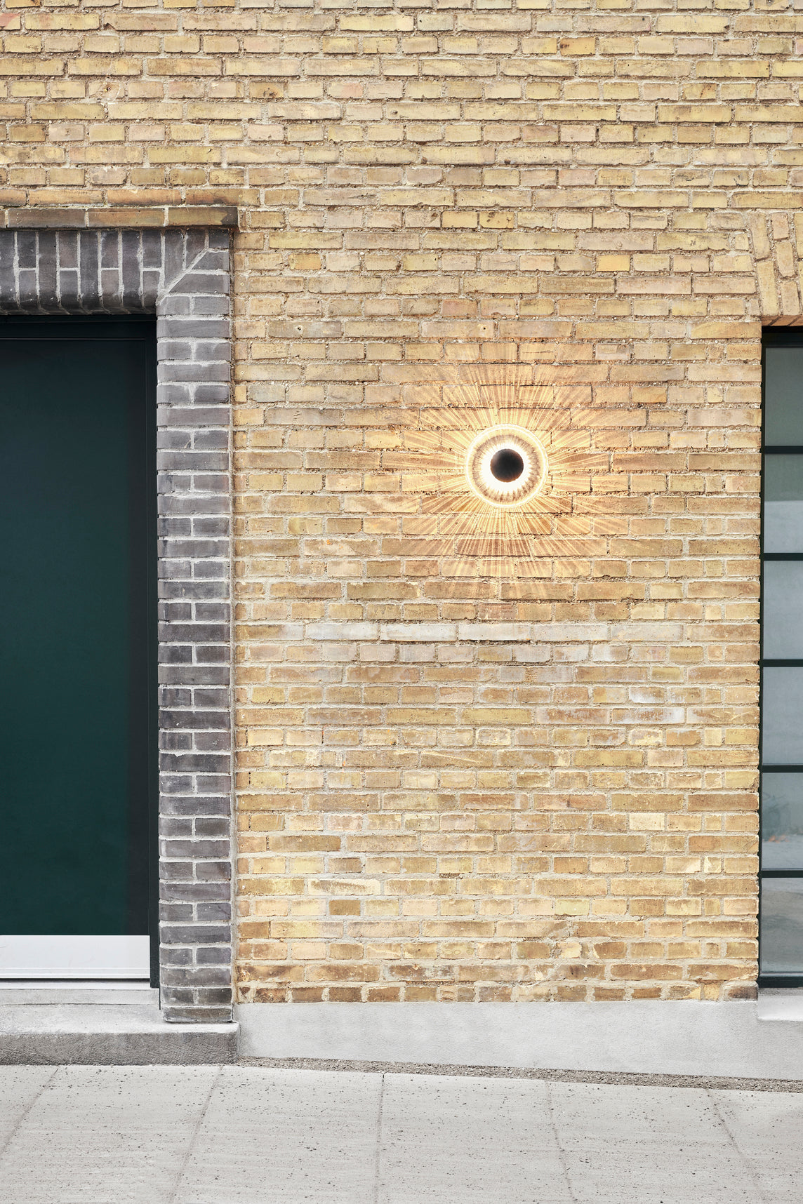 Rund udendørs væglampe af klart glas, på mur af gule mursten