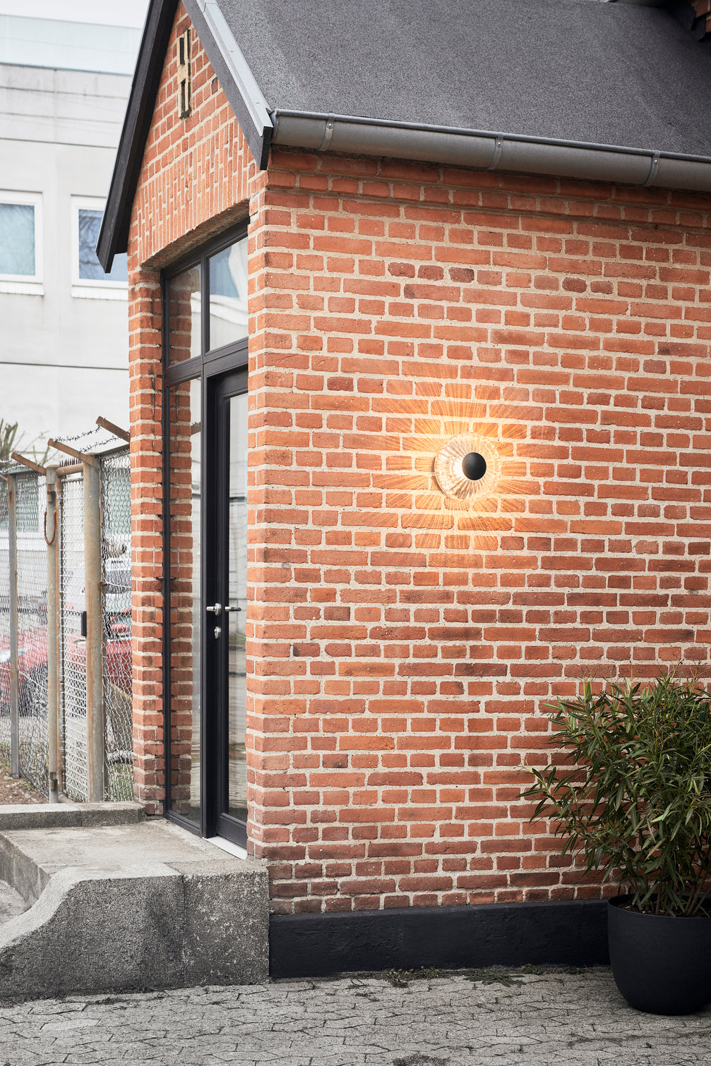 Rund udendørs væglampe af klart glas, på mur af røde mursten