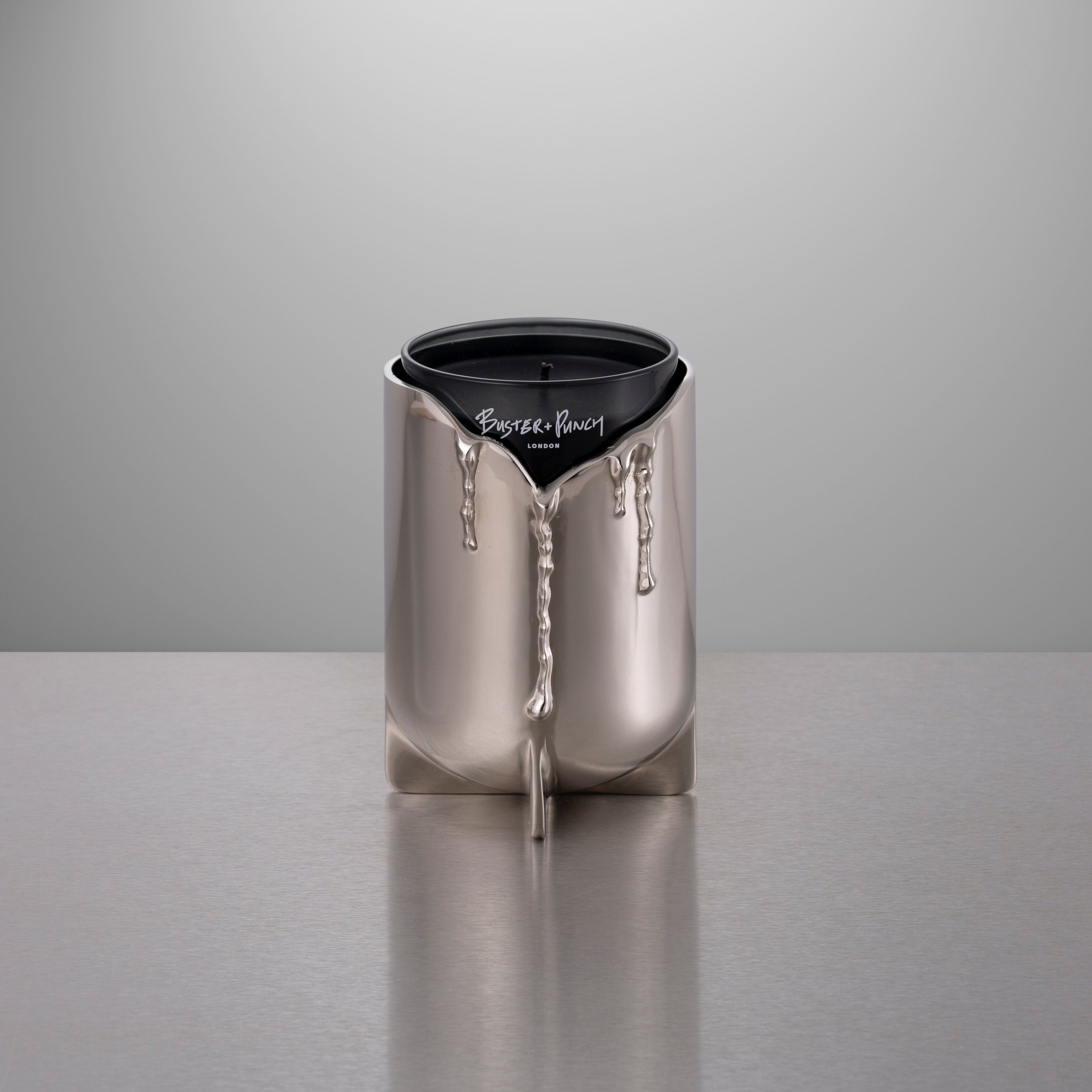 Lystage i stål med duftlys i glas, på grå baggrund.