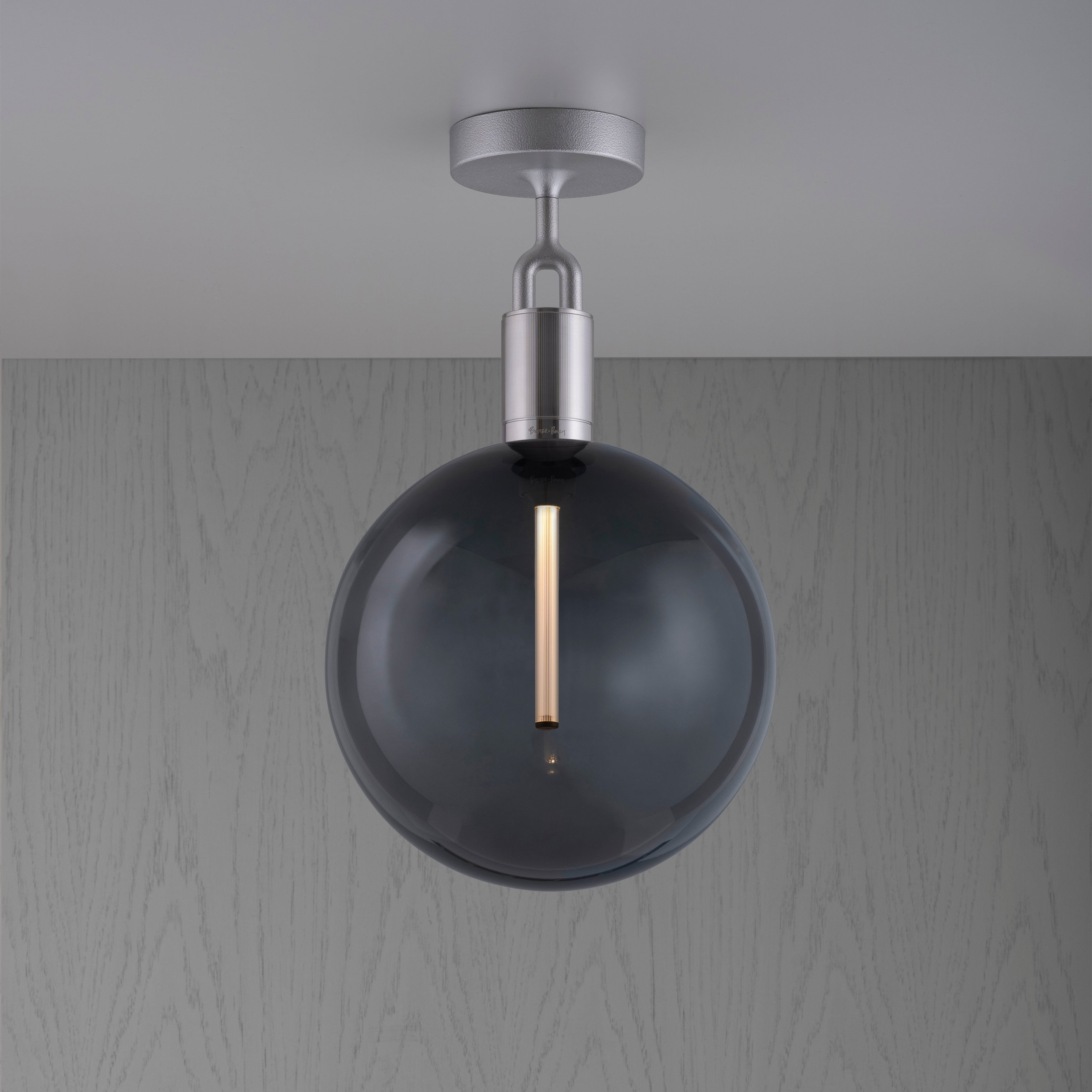 Loftlampe med rund skærm af røgfarvet glas og fatning af stål, på baggrund af gråt træ