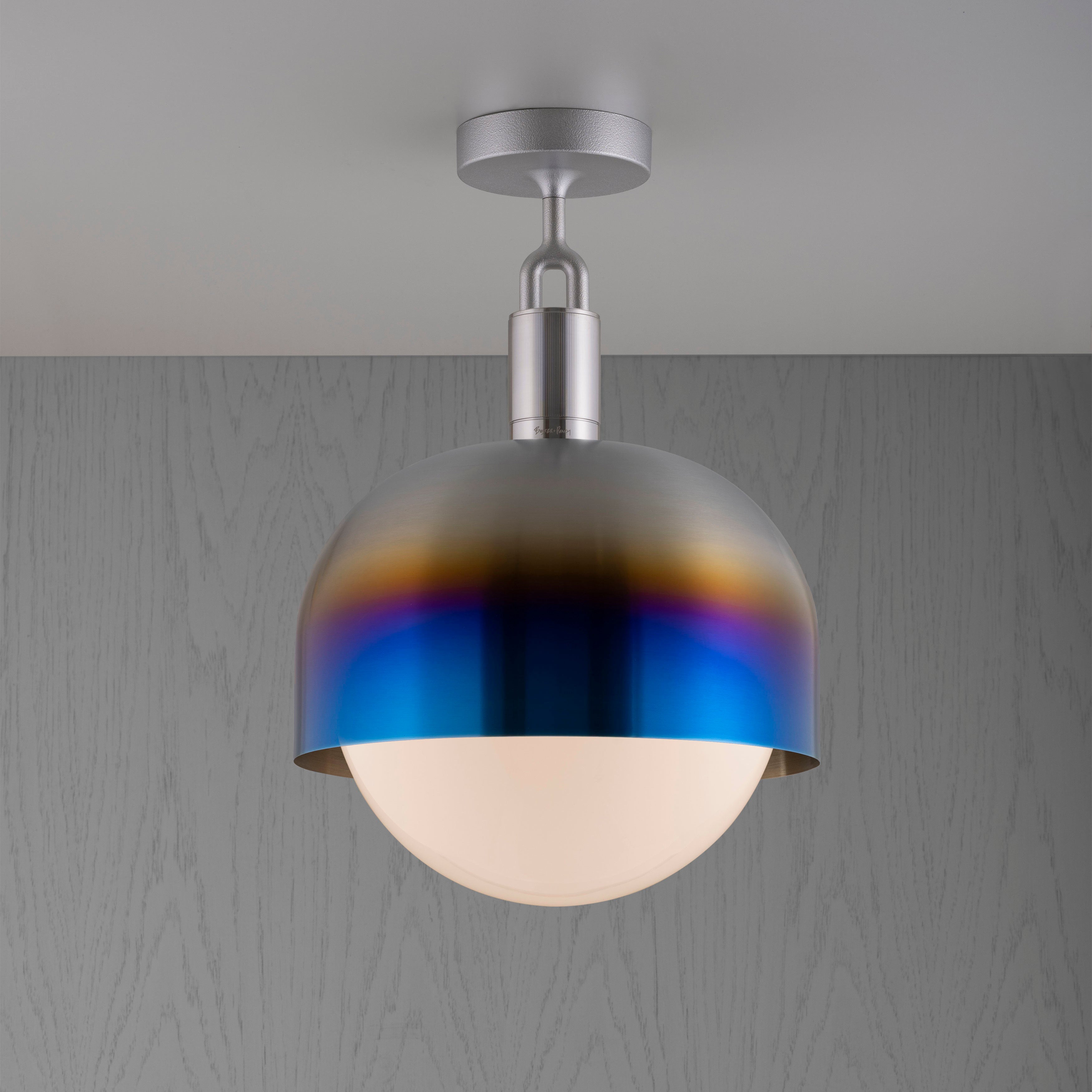 Loftlampe med fatning af stål samt skærm af brændt stål og pære af opalglas, på grå baggrund.