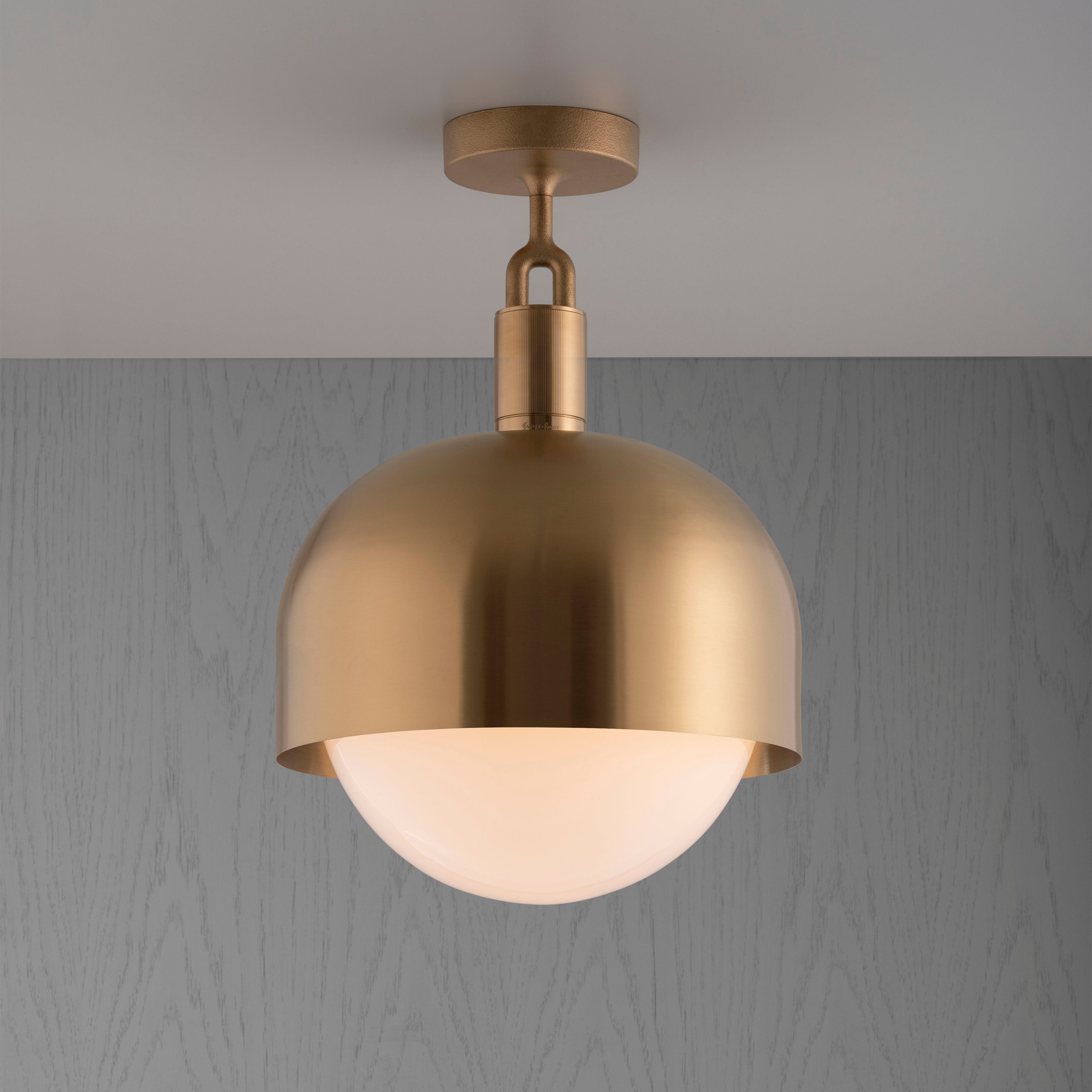 Loftlampe med fatning og skærm af messing samt pære i opalglas, på grå baggrund.