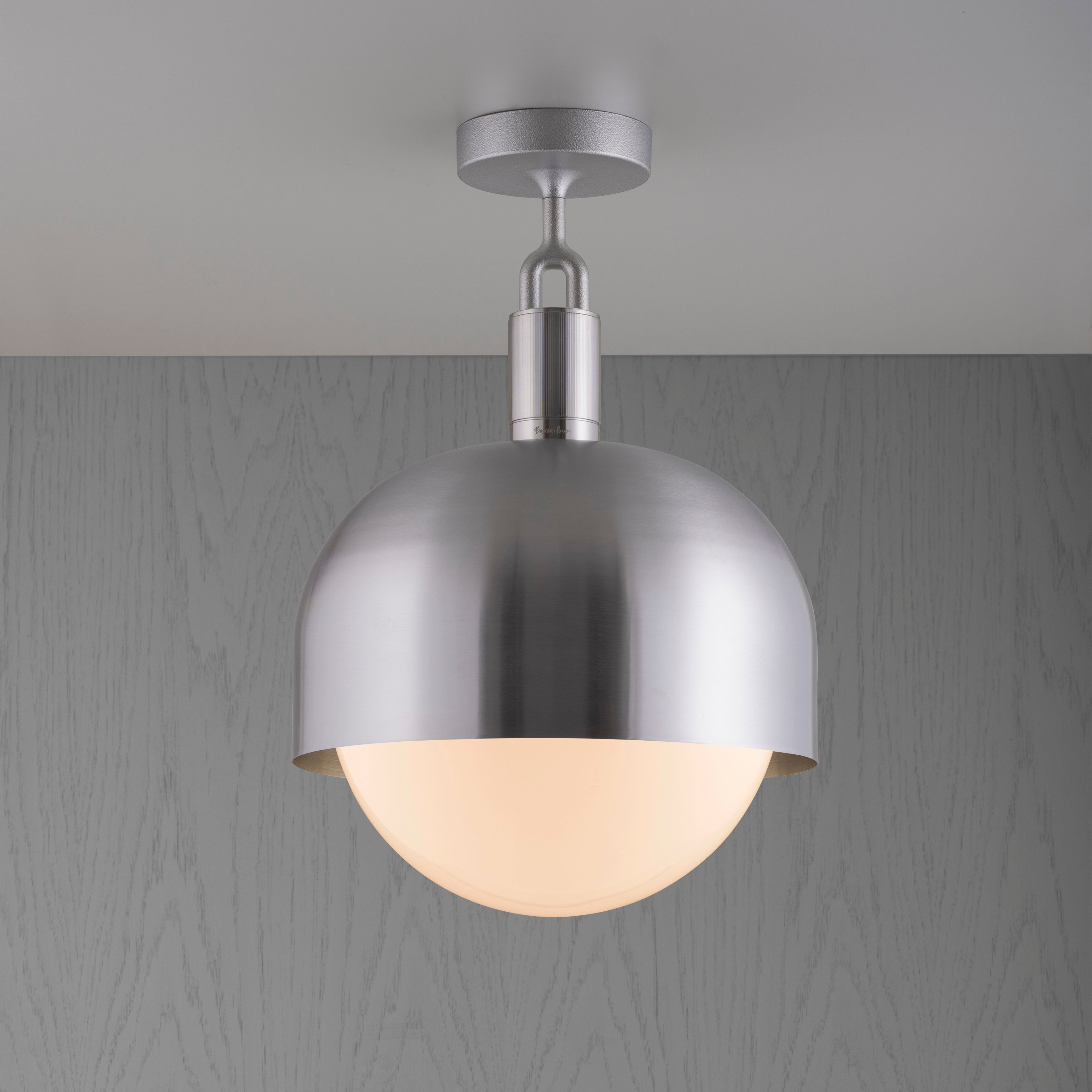 Loftlampe med fatning og skærm i stål samt pære i opalglas, på grå baggrund.