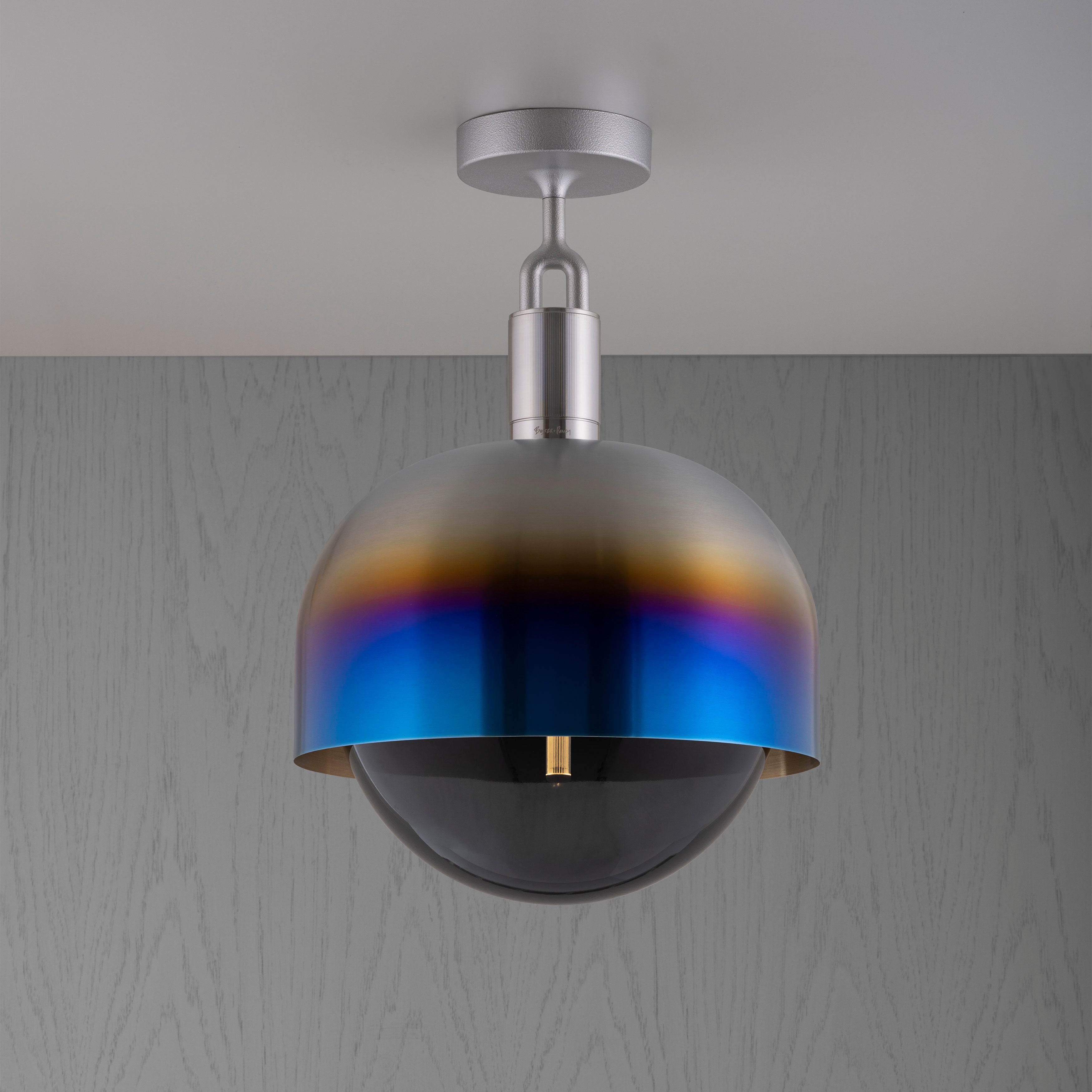 Loftlampe med fatning af stål samt skærm af brændt stål og pære af røgfarvet glas, på grå baggrund.