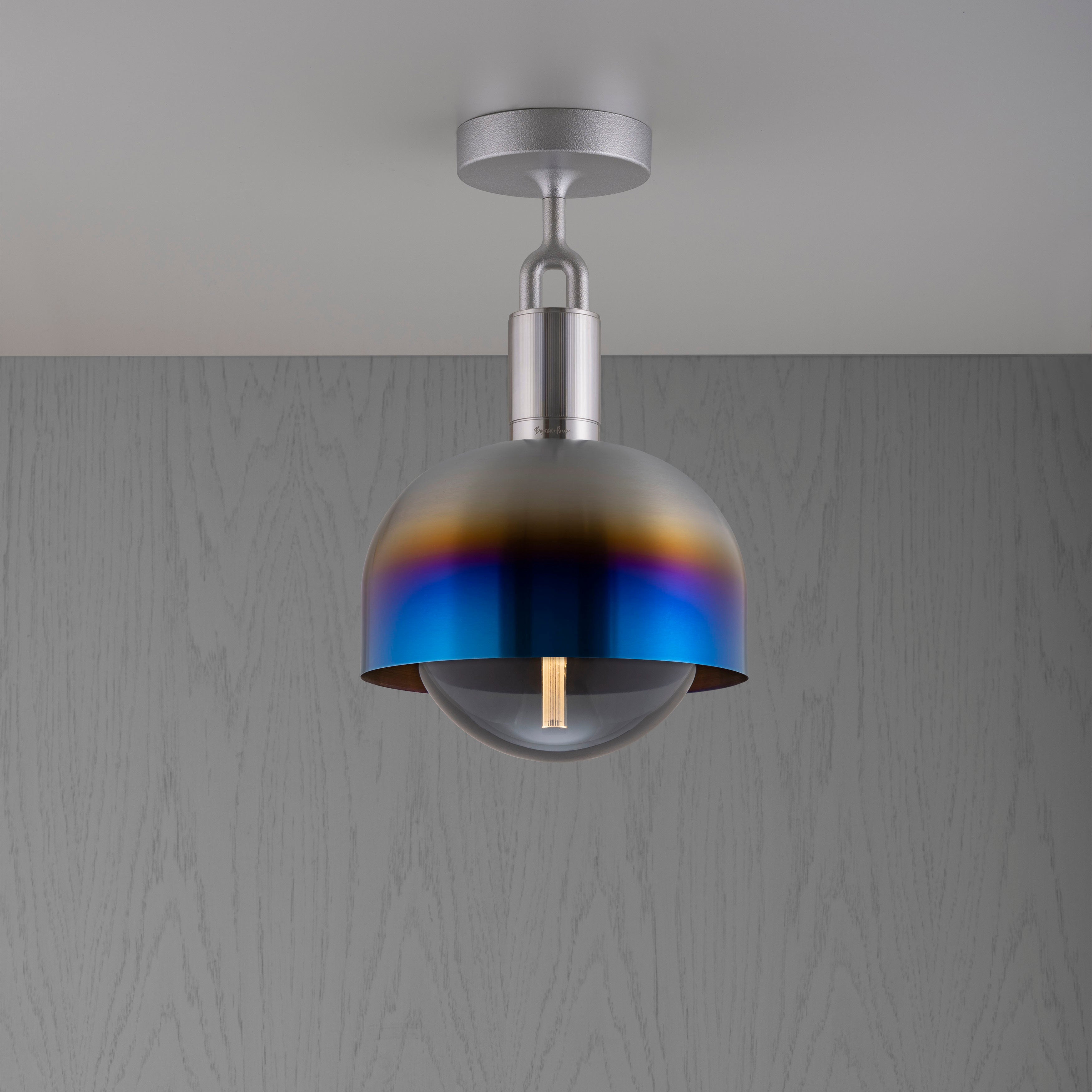 Loftlampe af stål og skærm af brændt stål samt røgfarvet pære, på grå baggrund.