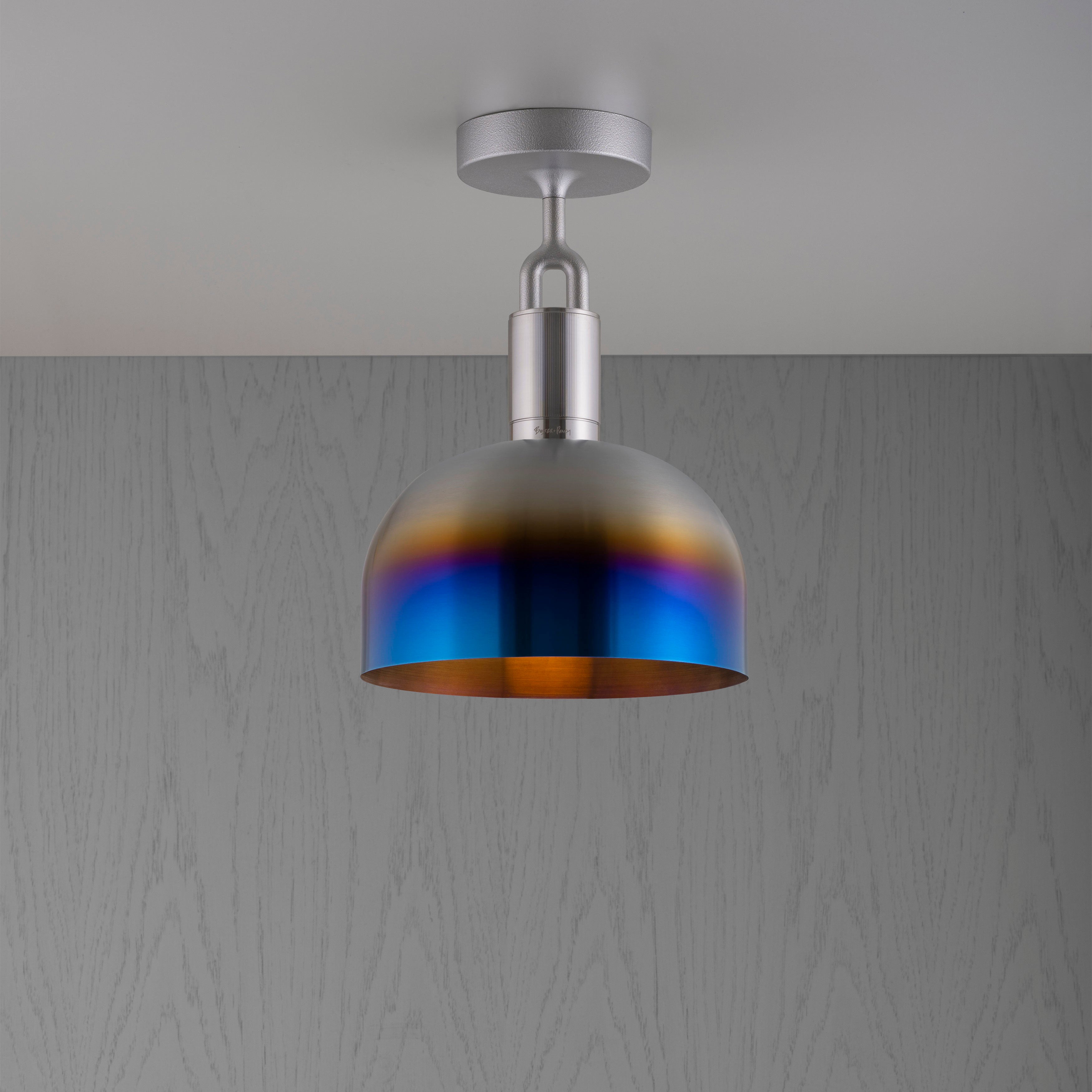 Loftlampe med fatning af stål og skærm af brændt stål, på grå træbaggrund.