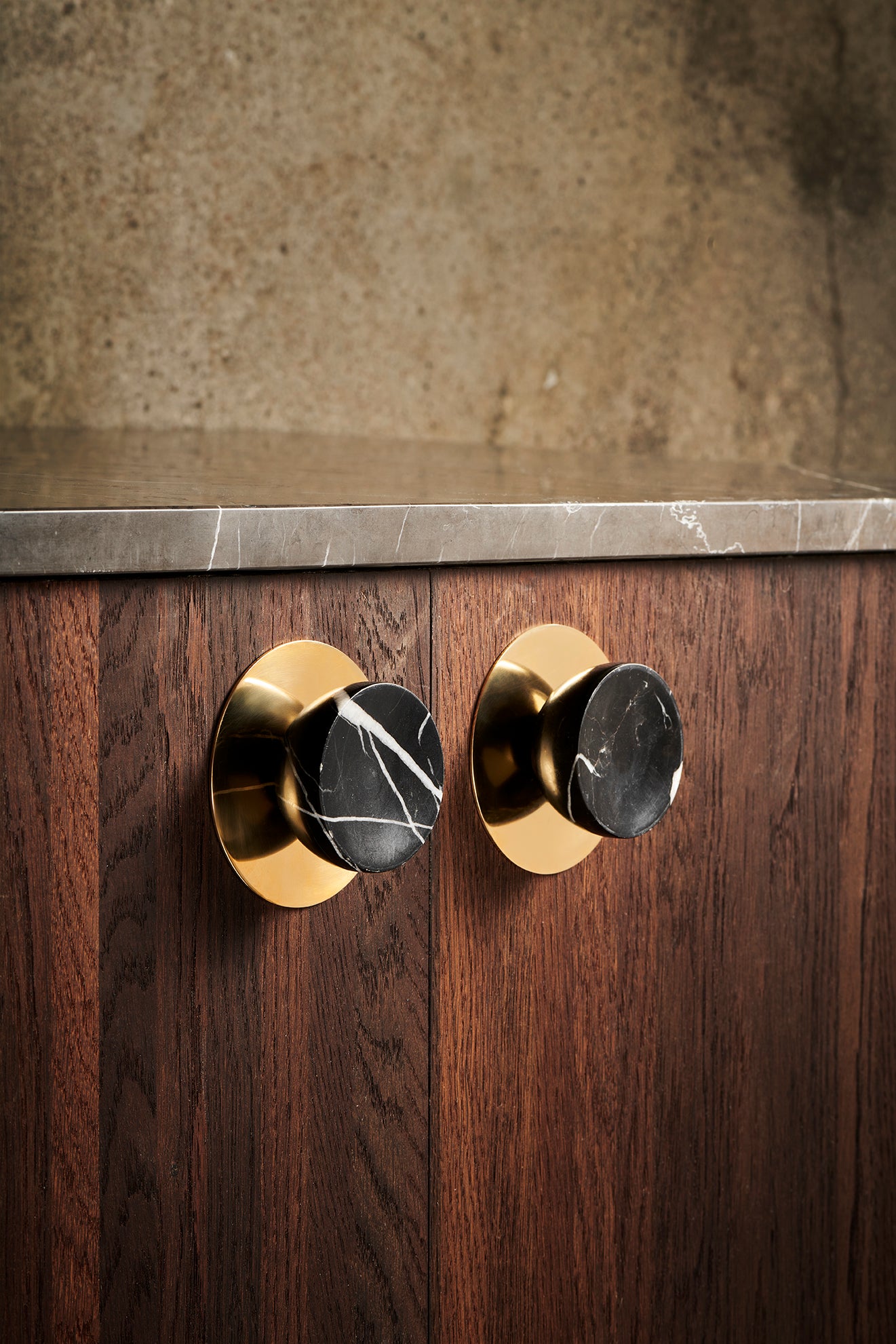 2 stk. runde og koniske møbelknopper i massiv sort marmor med hvide aftegninger. Her ses knopperne monteret på mørke træfronter med den runde messing bagplade, som kan tilkøbes.