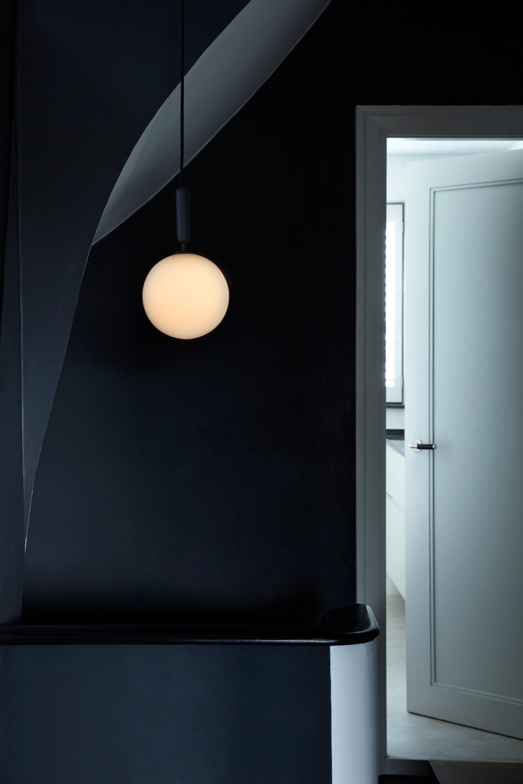 Pendel med rund skærm af opalglas og aflang grå fatning, i entre ved trappe