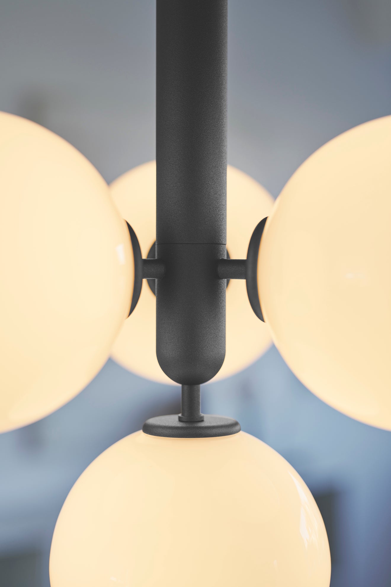 Close-up af pendel bestående af fire runde glasskærme af opalglas samt mørkegrå fatning