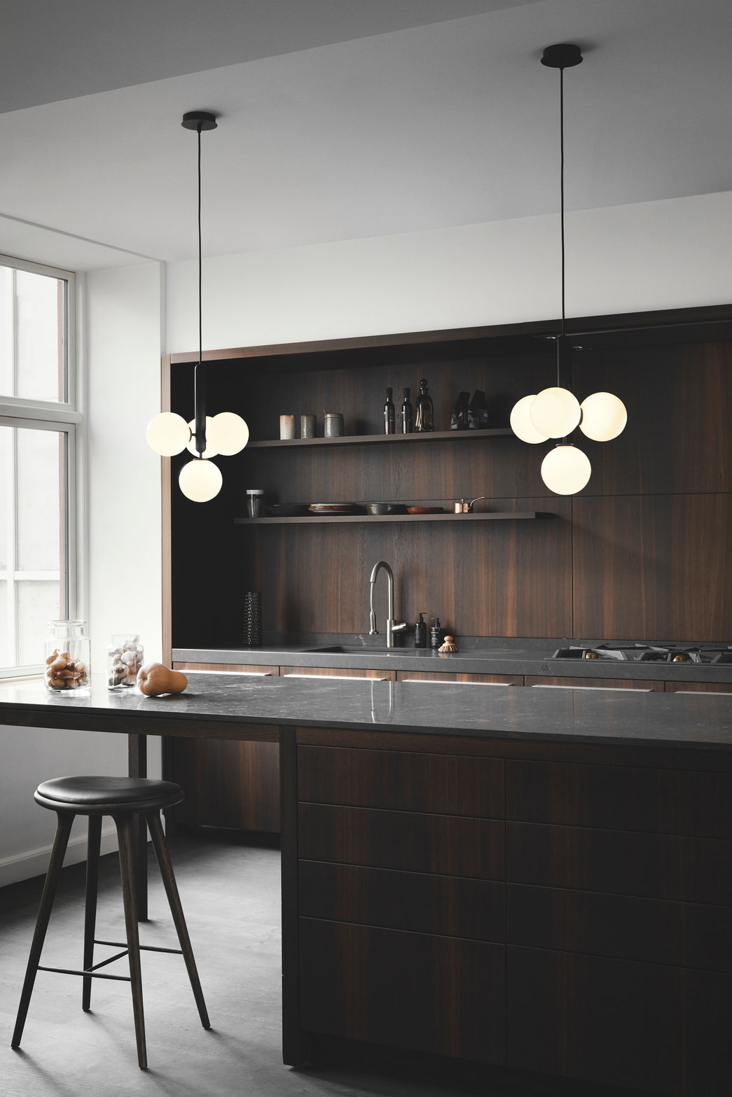 Pendel bestående af fire runde glasskærme af opalglas samt mørkegrå fatning, hængende over køkkenø i køkkenmiljø