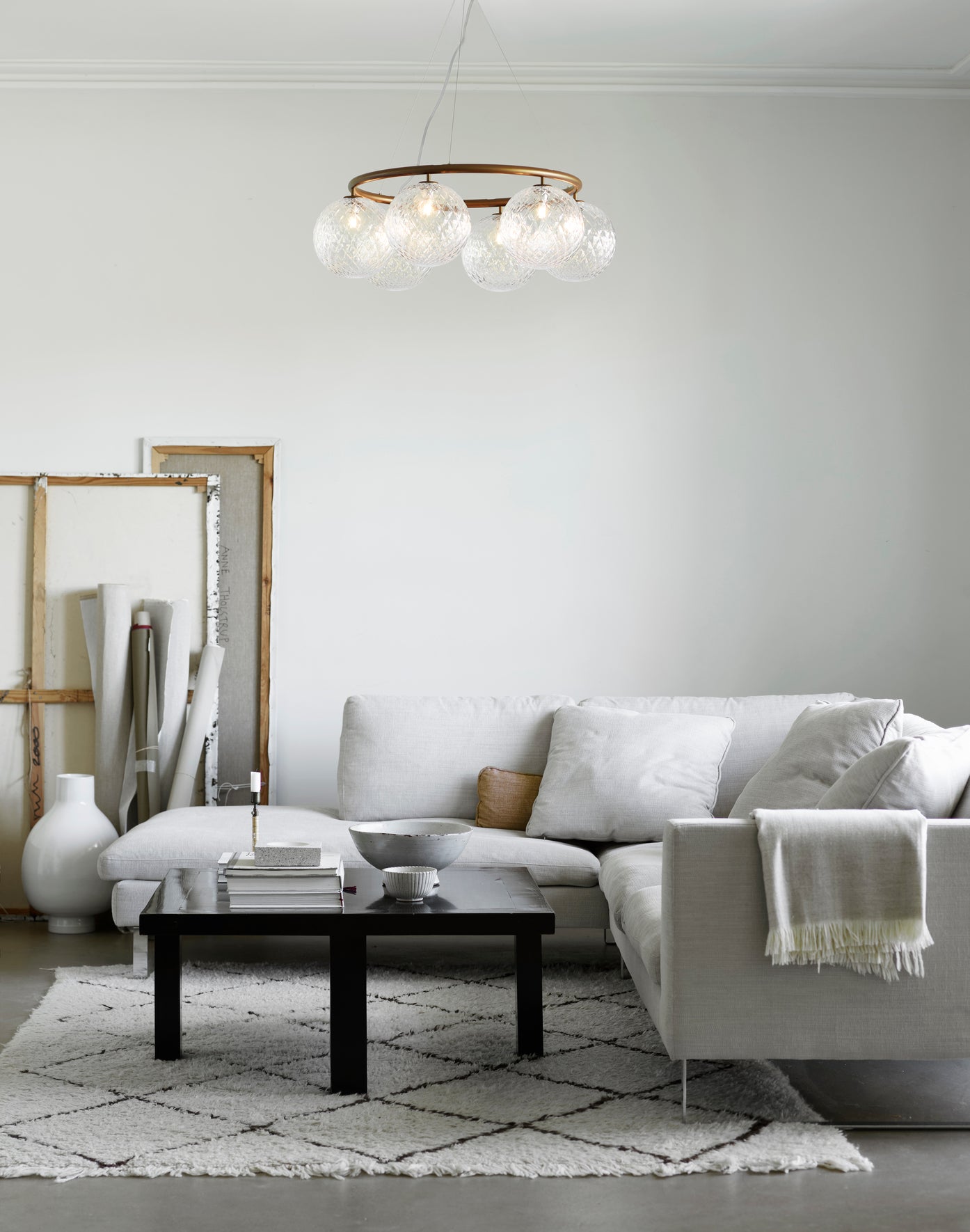 Lysekrone bestående af seks runde skærme i klart optikglas samt bruneret krone, i dagligstuemiljø