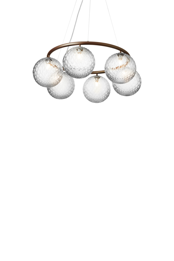 Lysekrone bestående af seks runde skærme i klart optikglas samt bruneret krone, på hvid baggrund