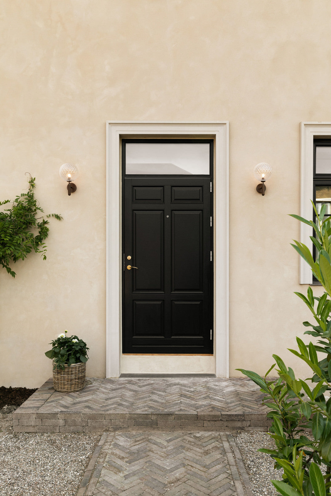 Væglamper med runde skærme af klart optikglas og bruneret stel, ved siden af hoveddør på gul mur