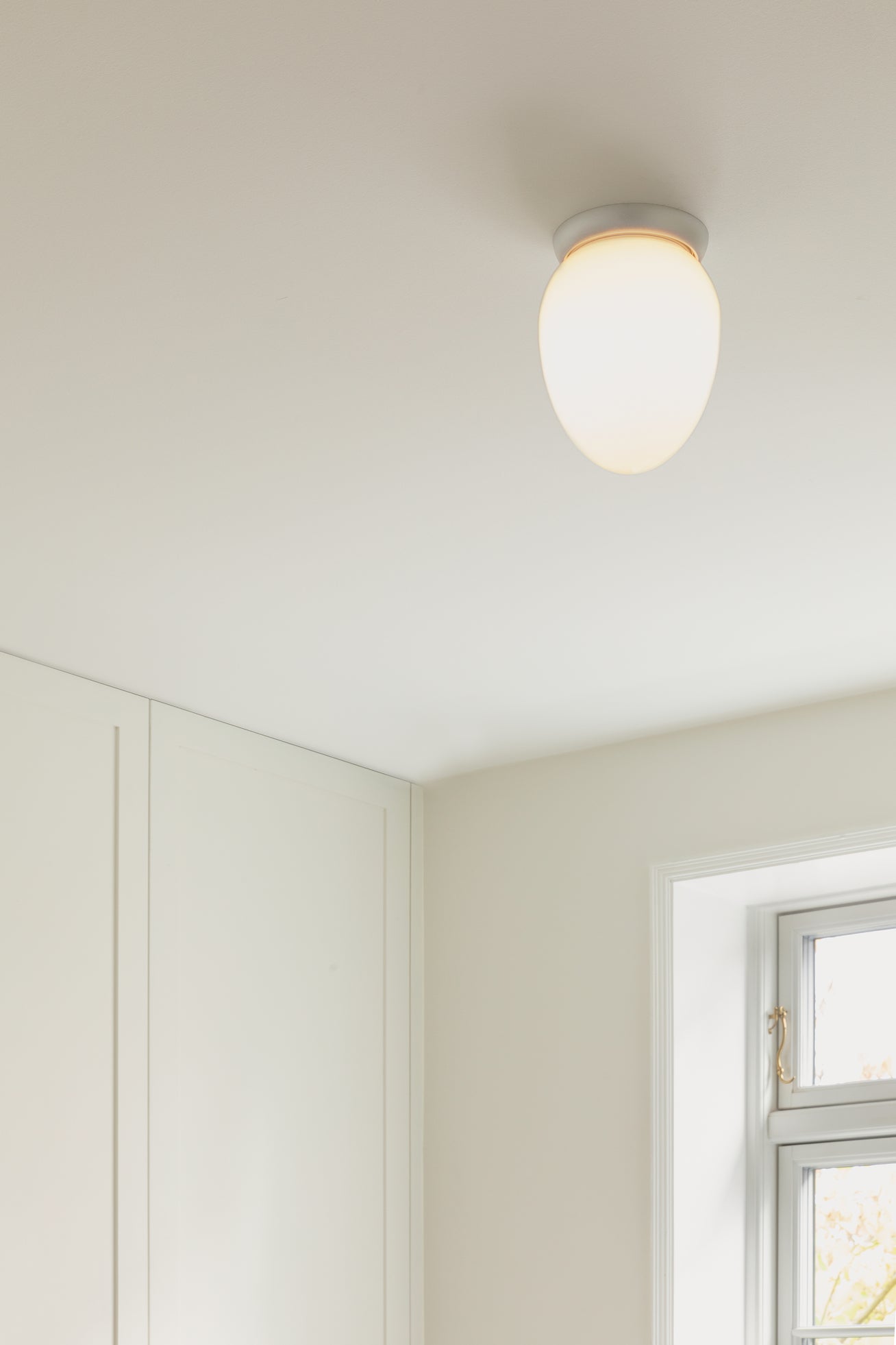 Loftlampe med sølvfarvet fatning og skærm af opalglas, på hvidt loft