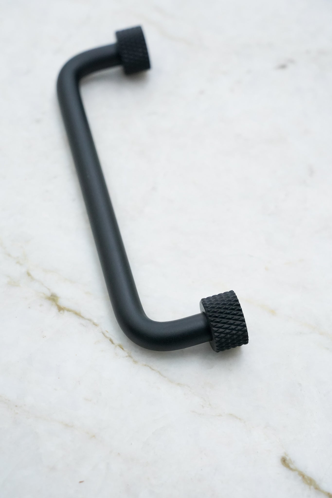 Køkkengreb i massiv messing med en mat sort overflade. Grebet har runde fødder med riflet diamond cut mønster, som matcher til quooker armatur.