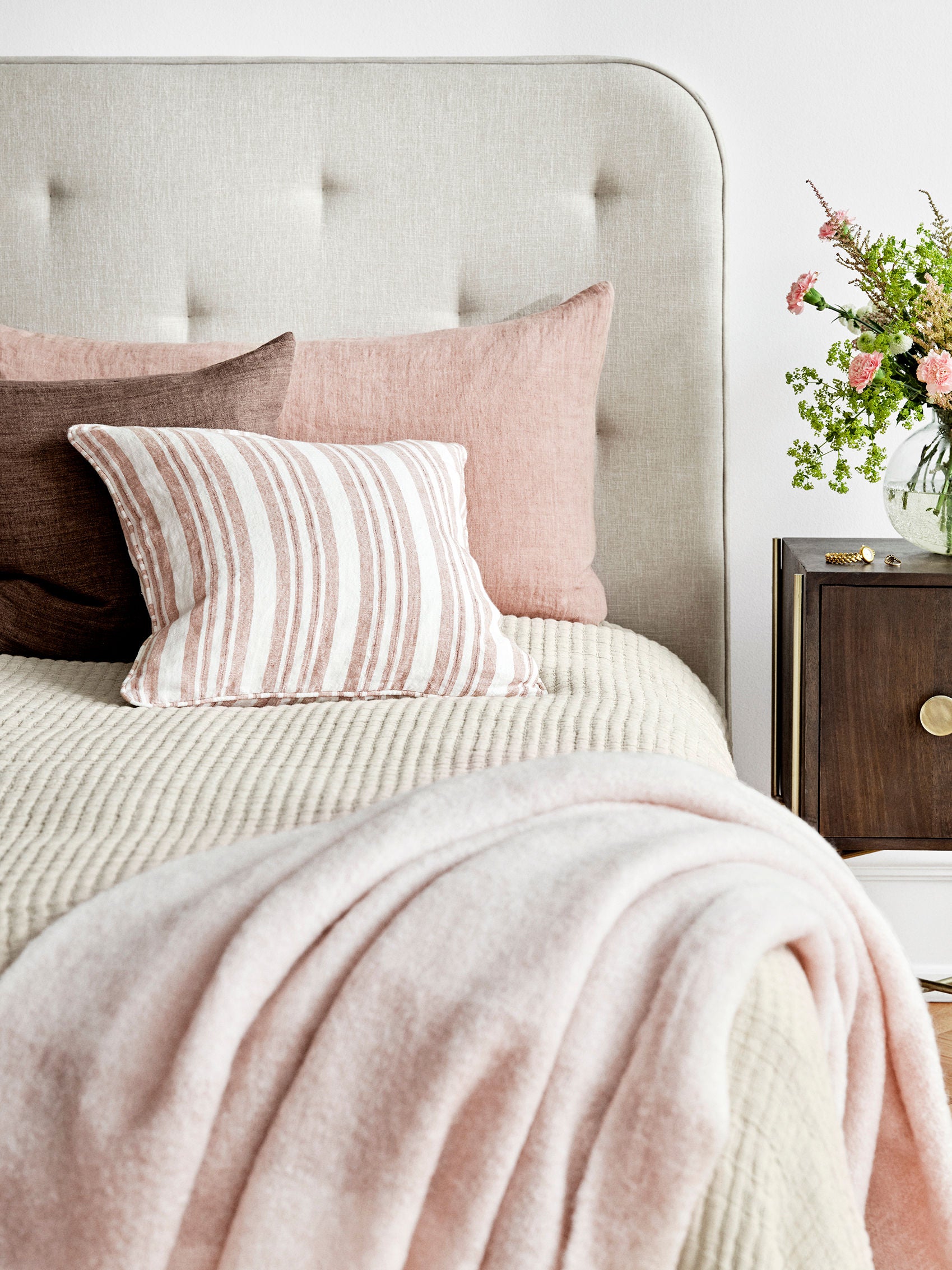 Tofarvet rosa uldplaid med lange frynser. Her ses plaiden liggende på en redt seng med matchende pyntepuder.