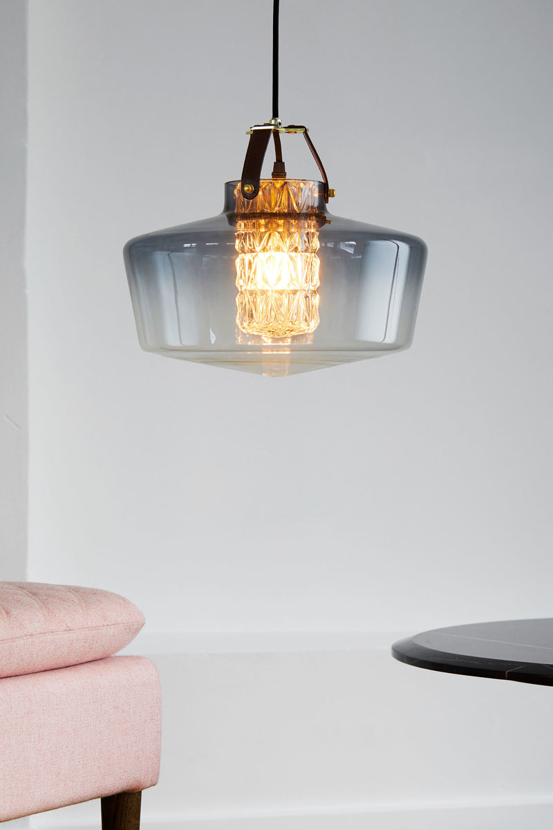 Lampen har en røgfarvet glasskærm i mundblæst glas, et facetslebet cylinderrør samt unikke detaljer i bl.a. læder.