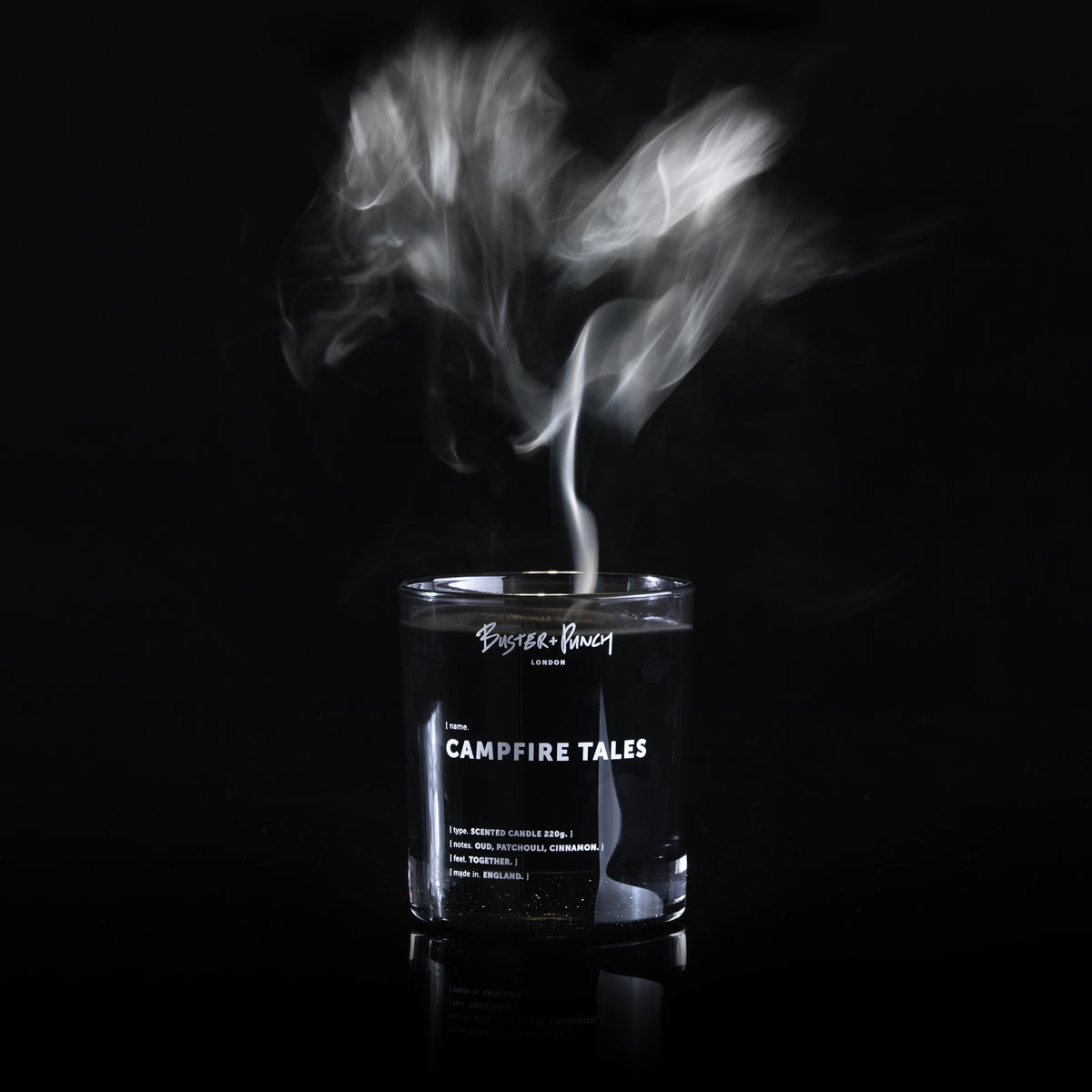 Duftlys af sort voks i røgfarvet glas med røg fra flamme, på sort baggrund.