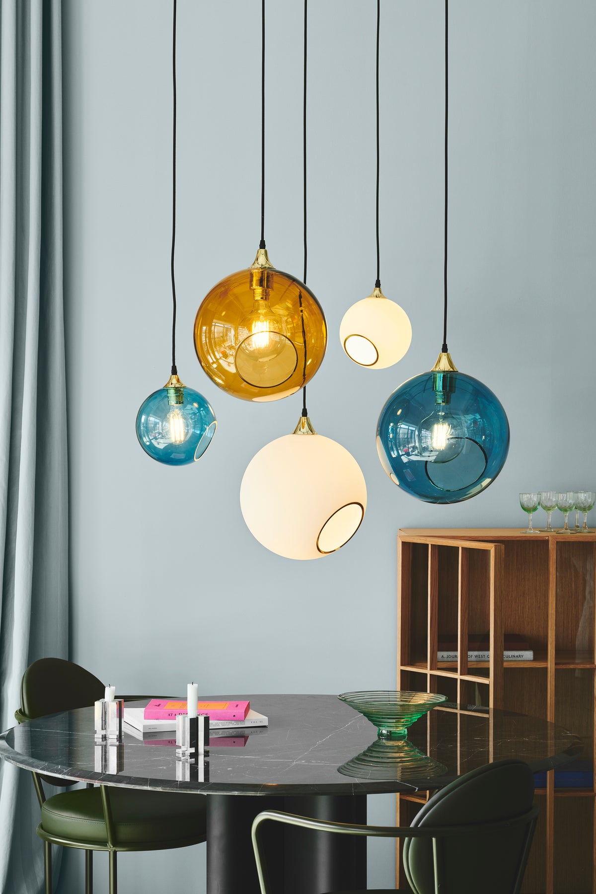 Runde Leuchte aus weißem Glas mit einer ausgeschnittenen Öffnung mit Goldrand und Blick auf das Leuchtmittel. Fassung und Deckenrosette sind goldfarben, das Kabel ist mit schwarzem Stoff ummantelt.