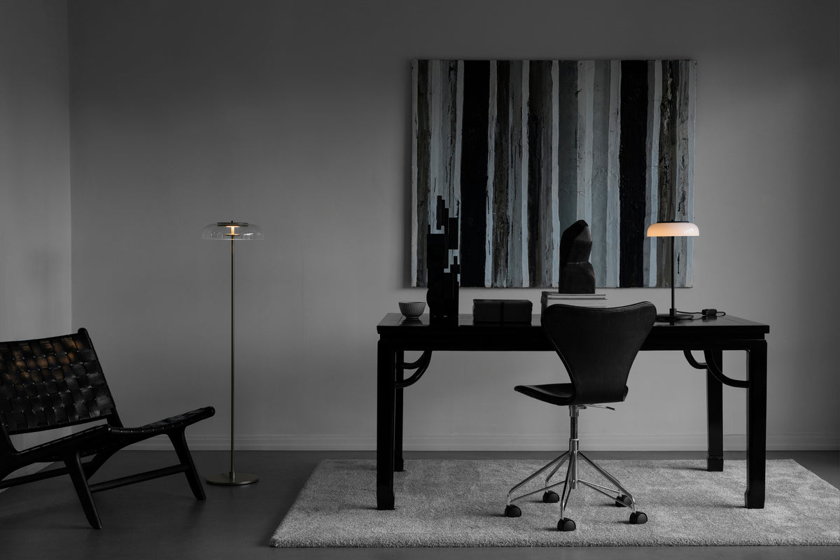 Gulvlampe med gyldent stel og fatning samt klar glasskærm, i kontormiljø