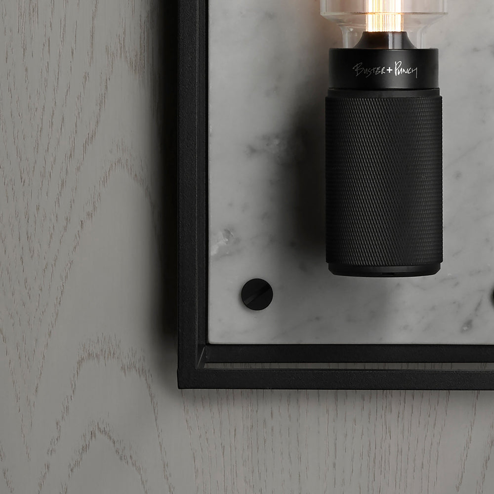 Buster and Punch caged wall lamp medium i sort metal med bagpanel i hvid marmor.