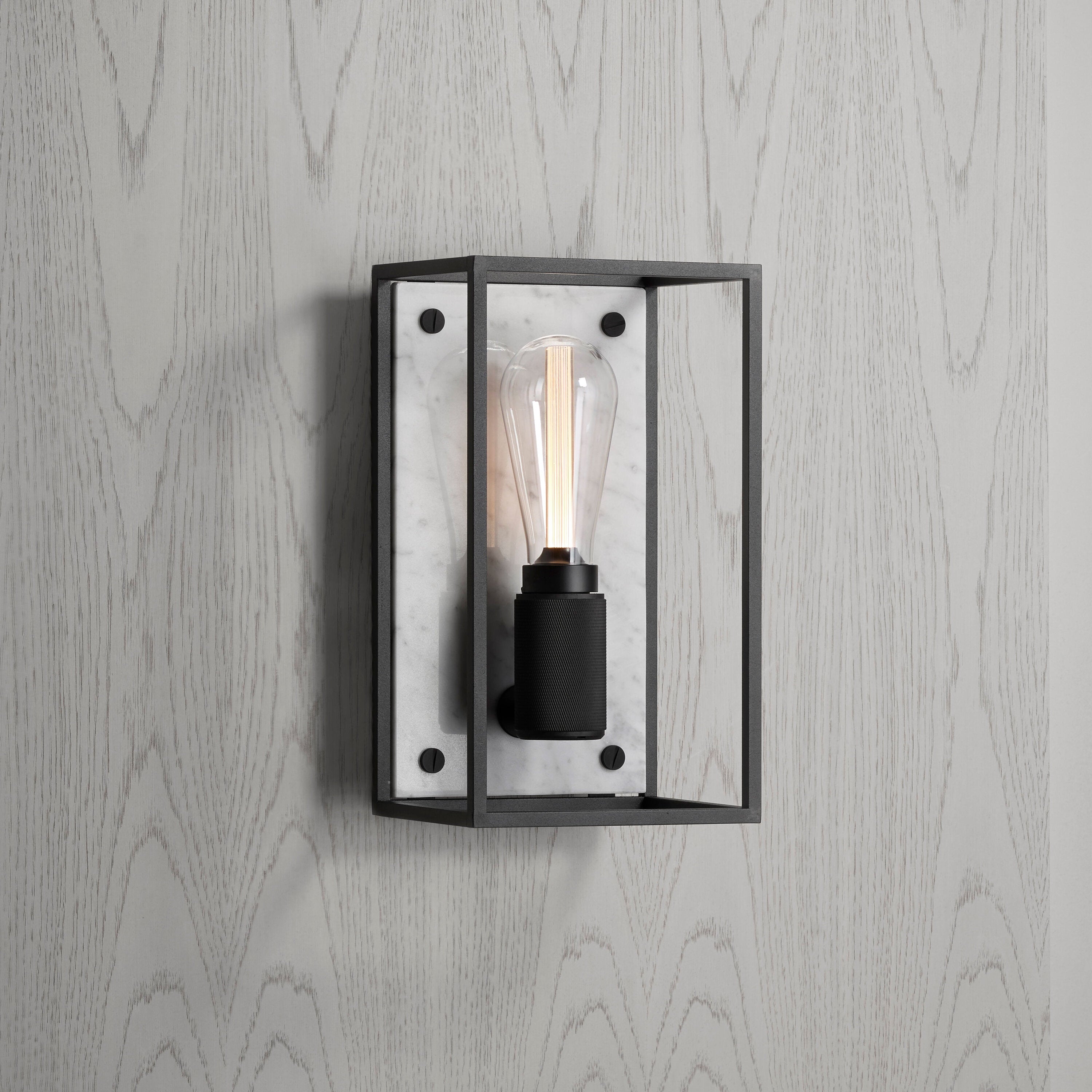 Buster and Punch caged wall lamp medium i sort metal med bagpanel i hvid marmor.