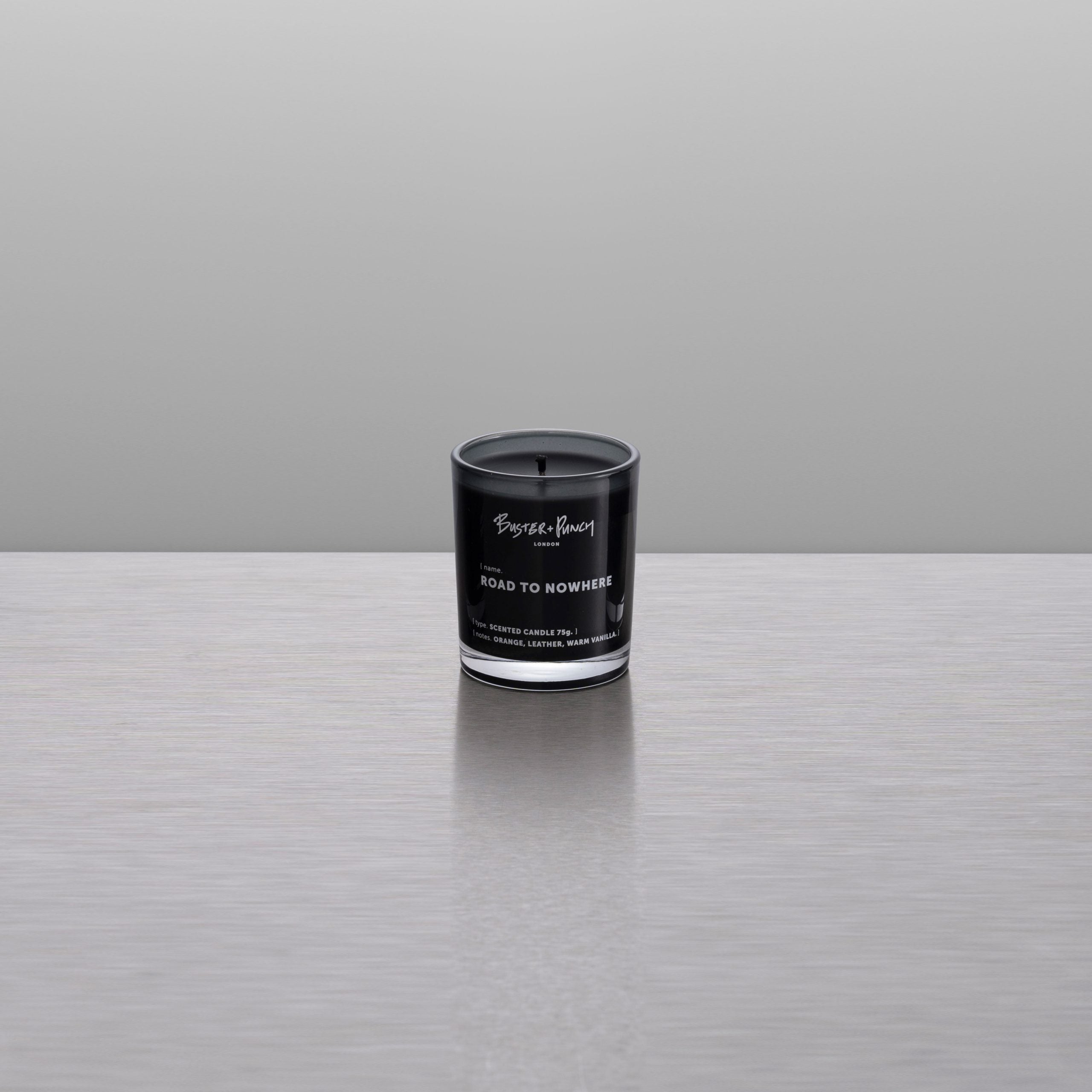 Duftlys af sort voks i røgfarvet glas, på grå baggrund.