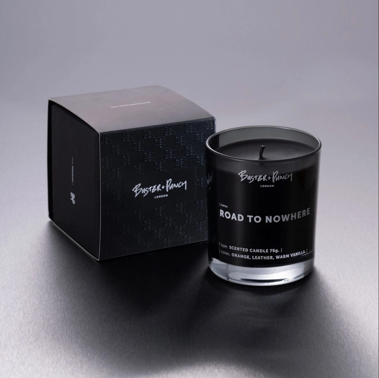 Æske indeholdende duftlys af sort voks i røgfarvet glas, på grå baggrund.