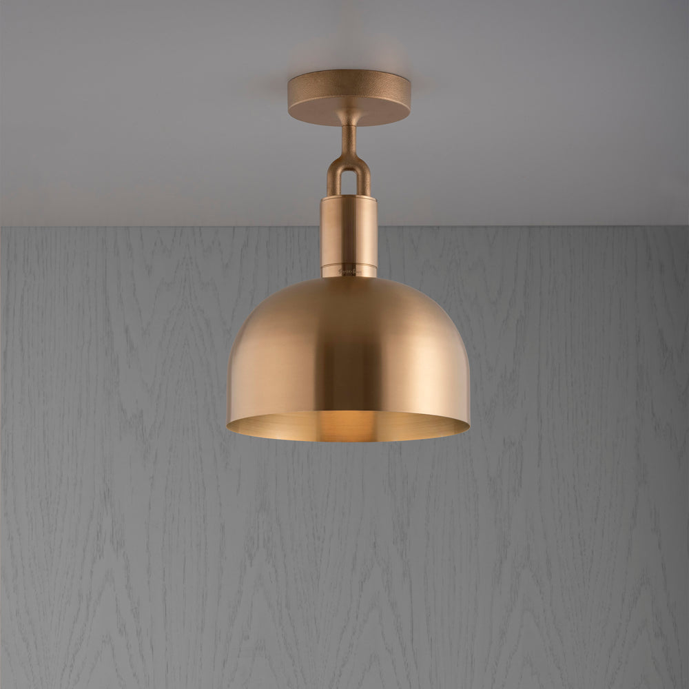 Loftlampe med skærm og fatning af messing, på grå træbaggrund.
