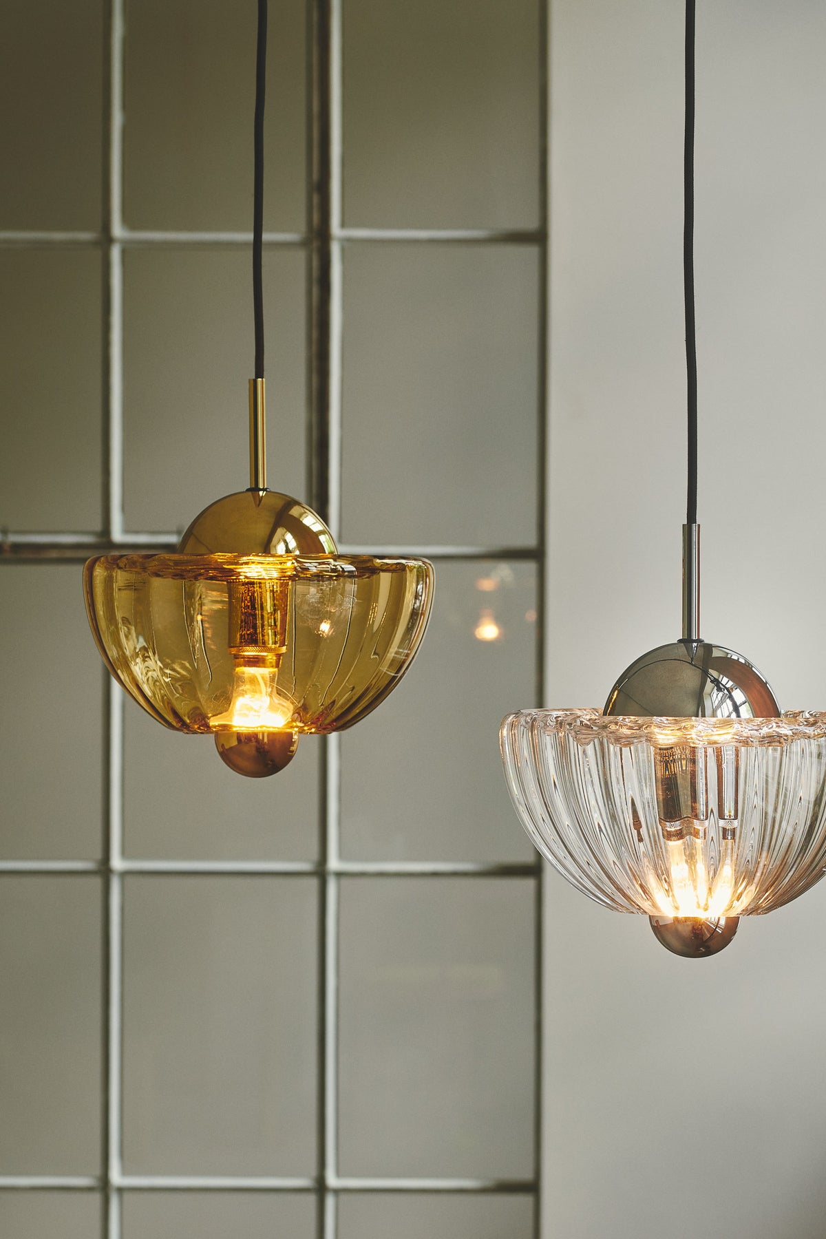 En klar Lotus pendel der hænger ved siden af en Lotus pendel i farven Amber.