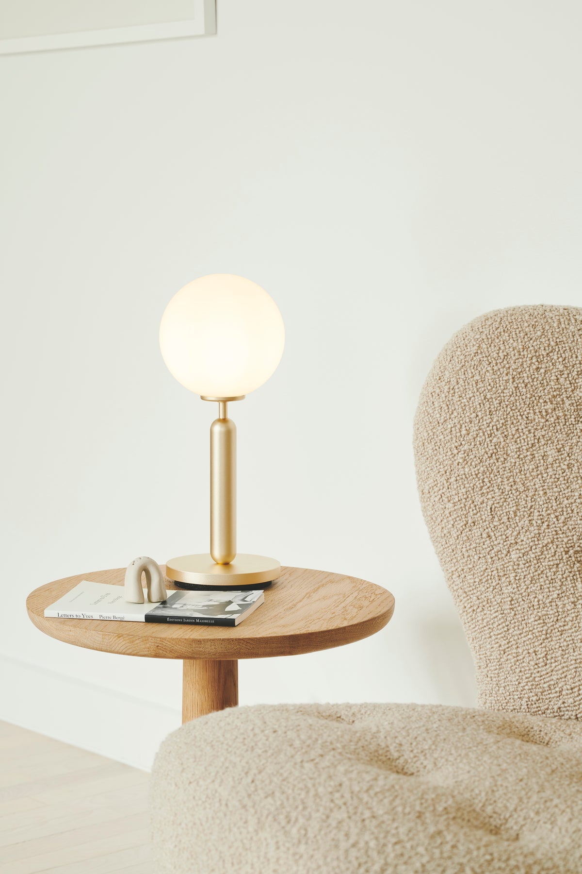 Bordlampe med rund skærm af opalglas og messingfarvet stel, ved sidebord i dagligstuemiljø