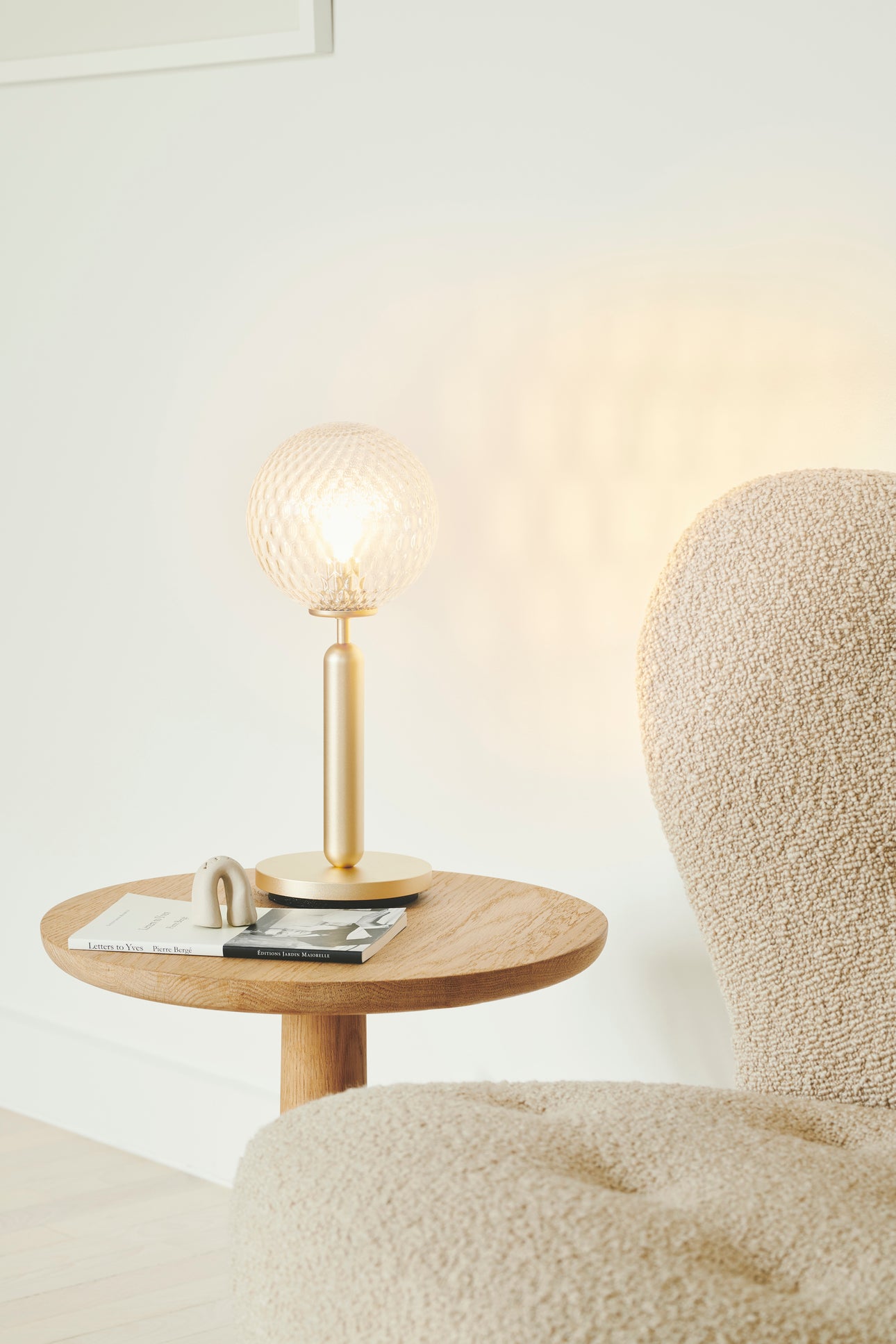 Bordlampe med rund skærm af klart optikglas og mørkegråt stel, på sidebord i dagligstuemiljø