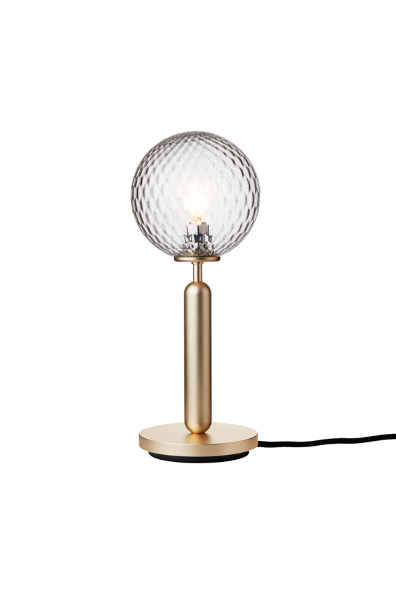 Bordlampe med rund skærm af klart optikglas og messingfarvet stel, på hvid baggrund