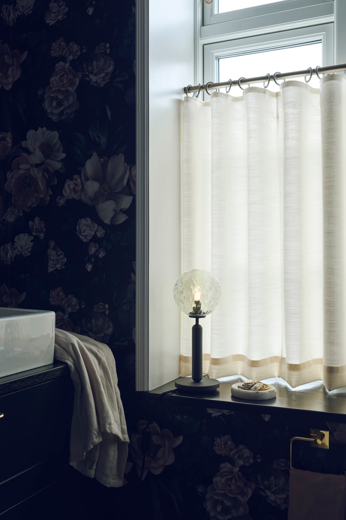 Bordlampe med rund skærm af klart optikglas og mørkegråt stel, i vindueskarm på badeværelse