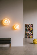 Rund væglampe i amber plisseret glas, som skaber et lysspil på væggen. 