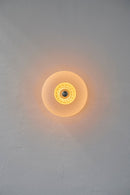 Rund væglampe i amber plisseret glas, som skaber et lysspil på væggen. 