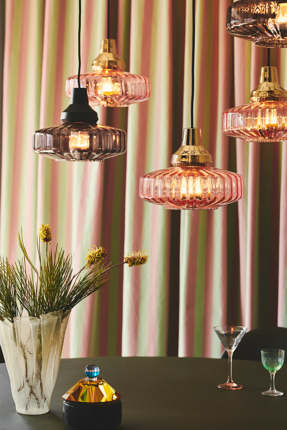 Pendel lampe fra Design by Us i lyserød glas og med guldfarvet fatning og bagstykke.