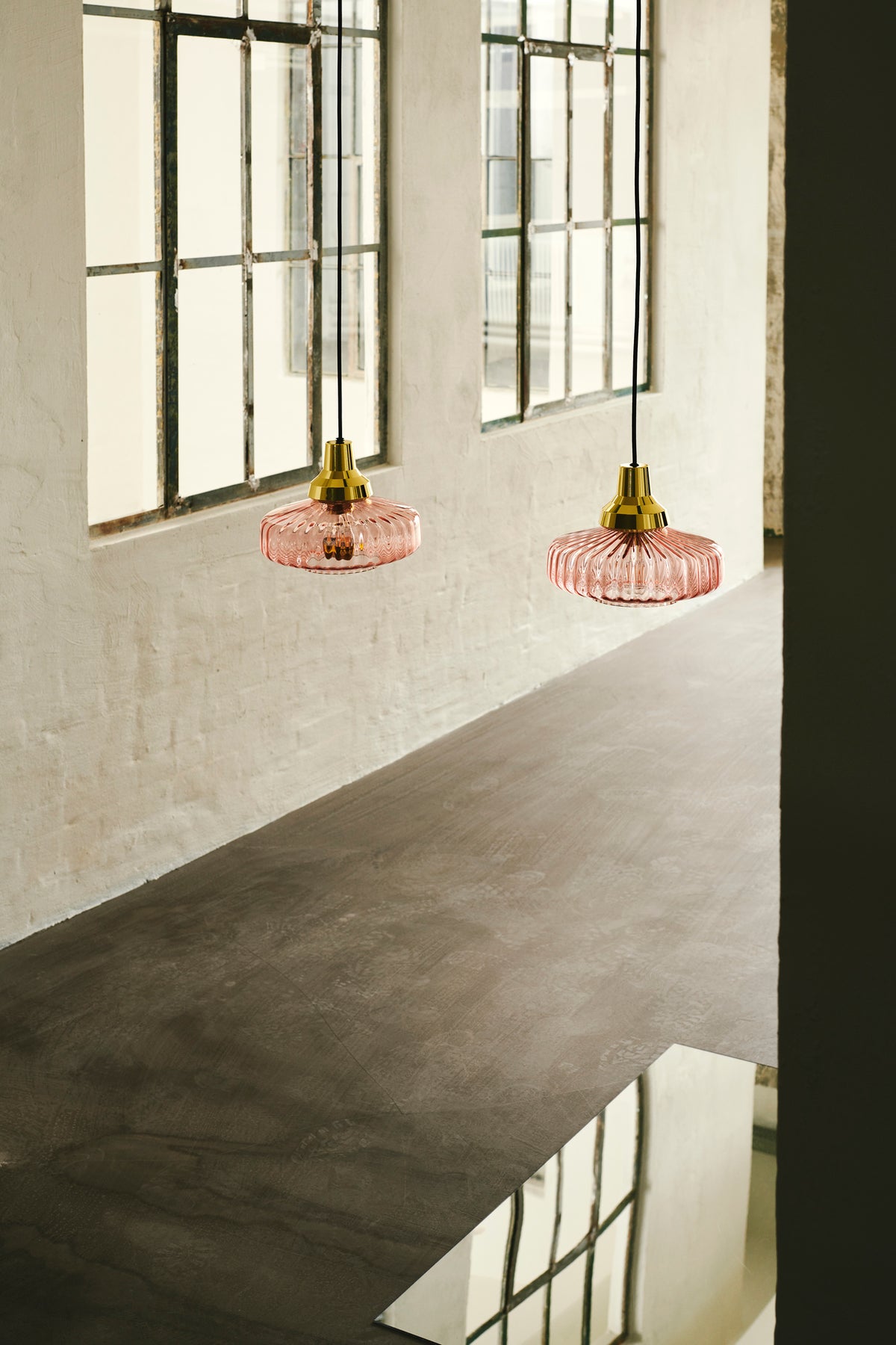 Pendel lampe fra Design by Us i lyserød glas og med guldfarvet fatning og bagstykke.